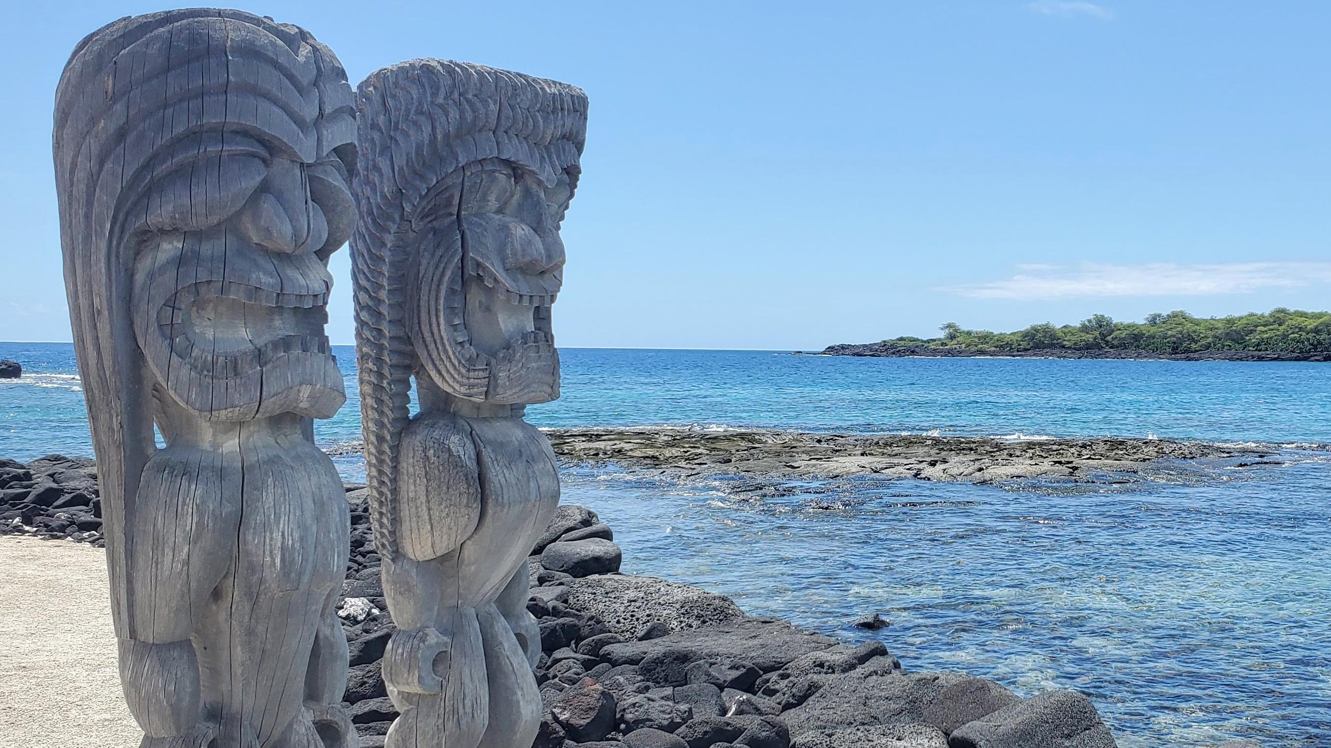 A pair of intricately carved kiʻi (temple images) stand facing Hōnaunau Bay