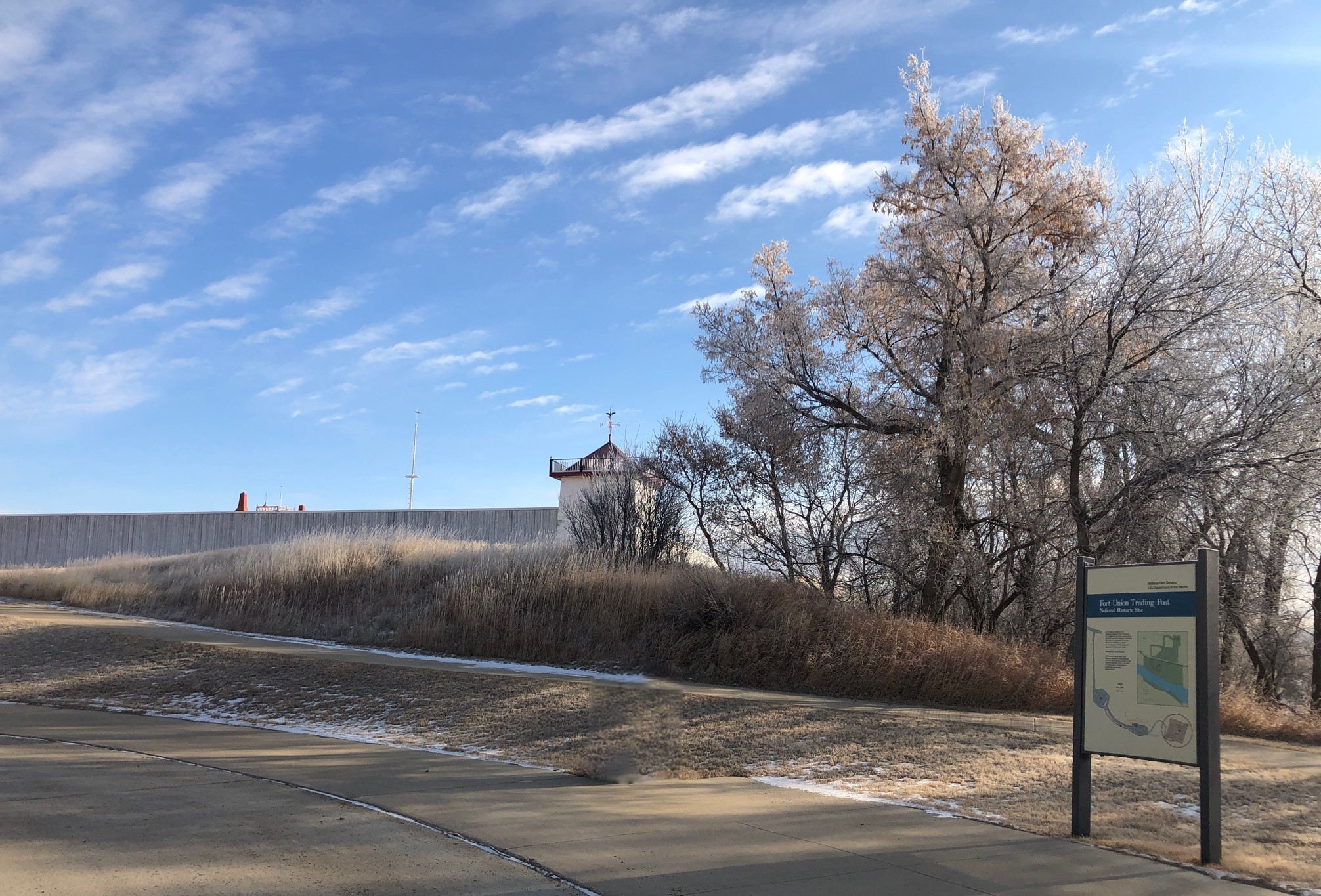 Exhibit at base of grassy hill, with trees and Fort wall and Bastion at crest of hill.
