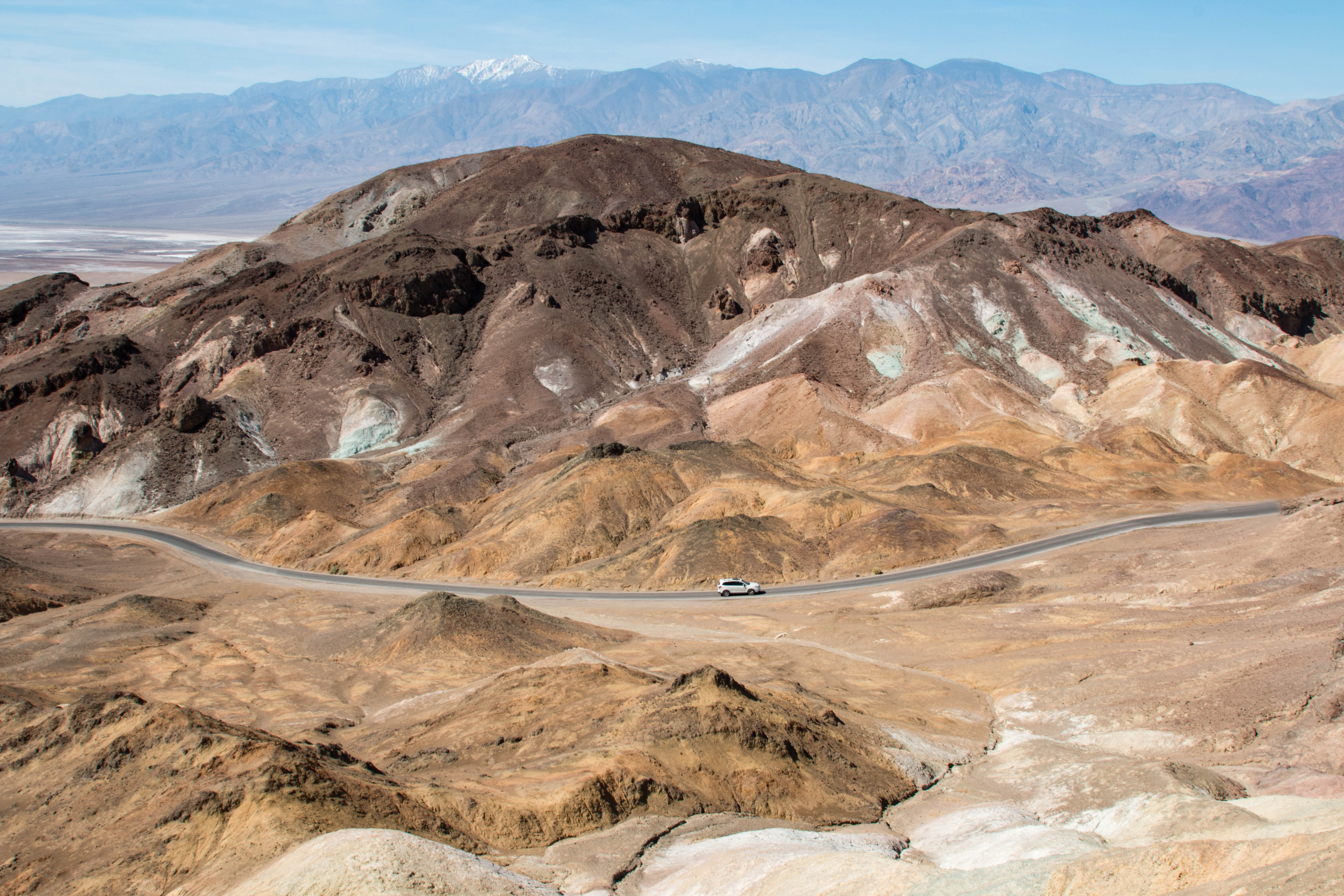Car driving on a windy one-way road between colorful brown and yellow hills.
