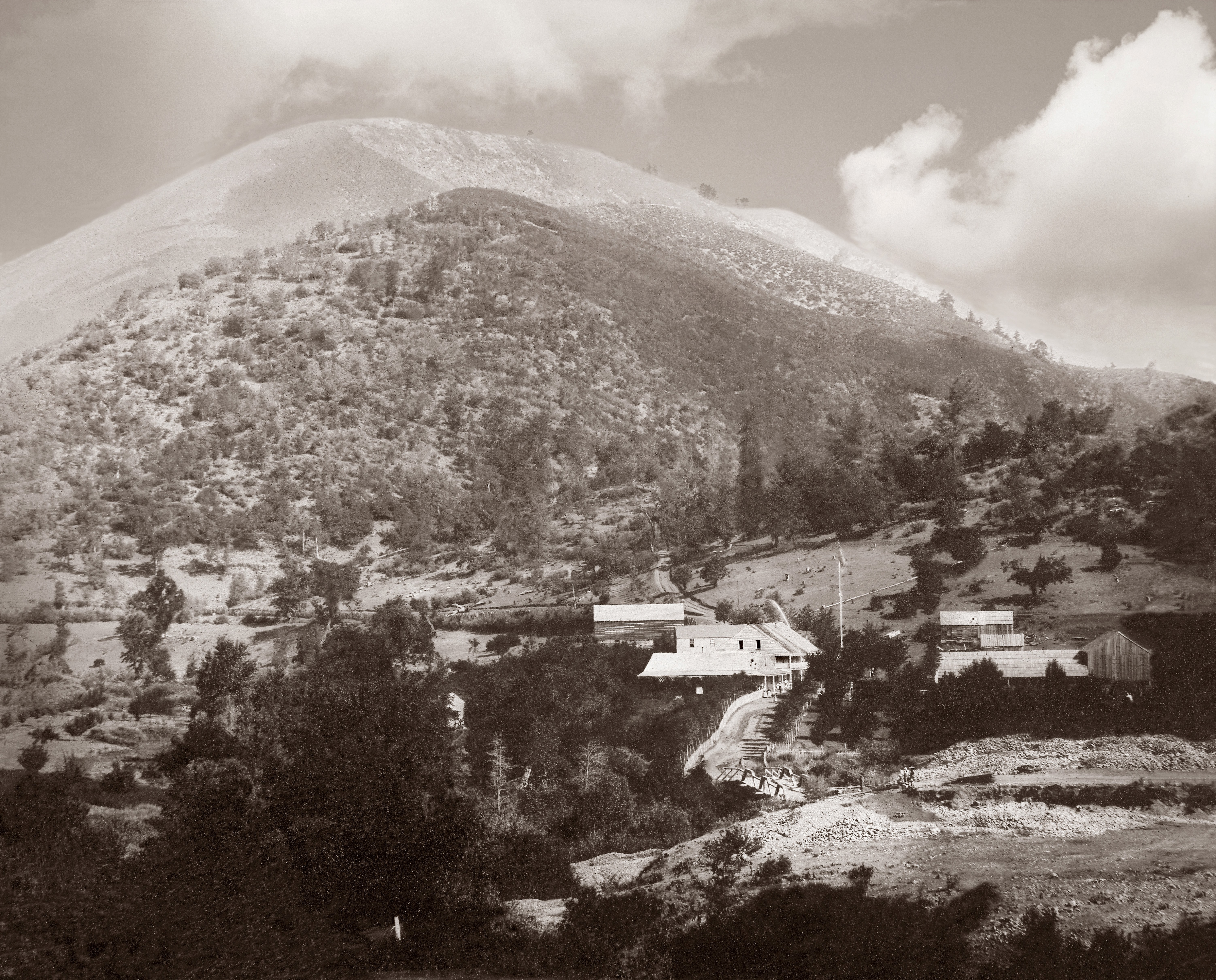 A collection of buildings in a pine and oak covered landscape with mountain in the background.