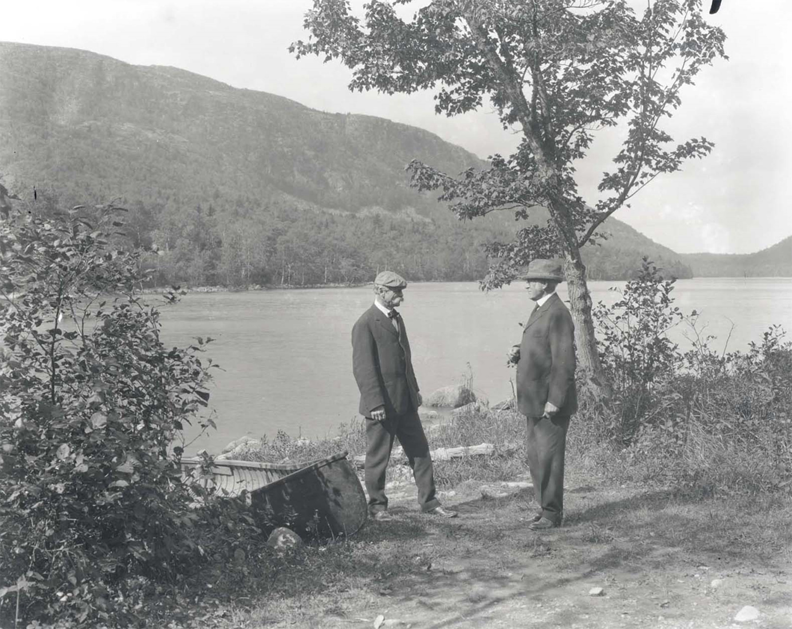 Two men stand in front of a lake.