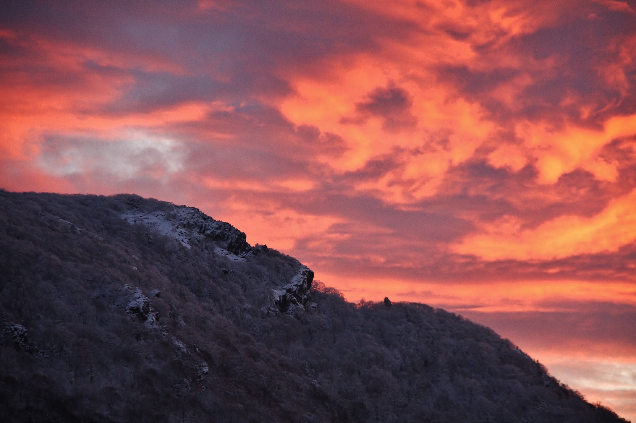 The profile of the mountain with bare trees, snow-covered rocks, and an orange sky