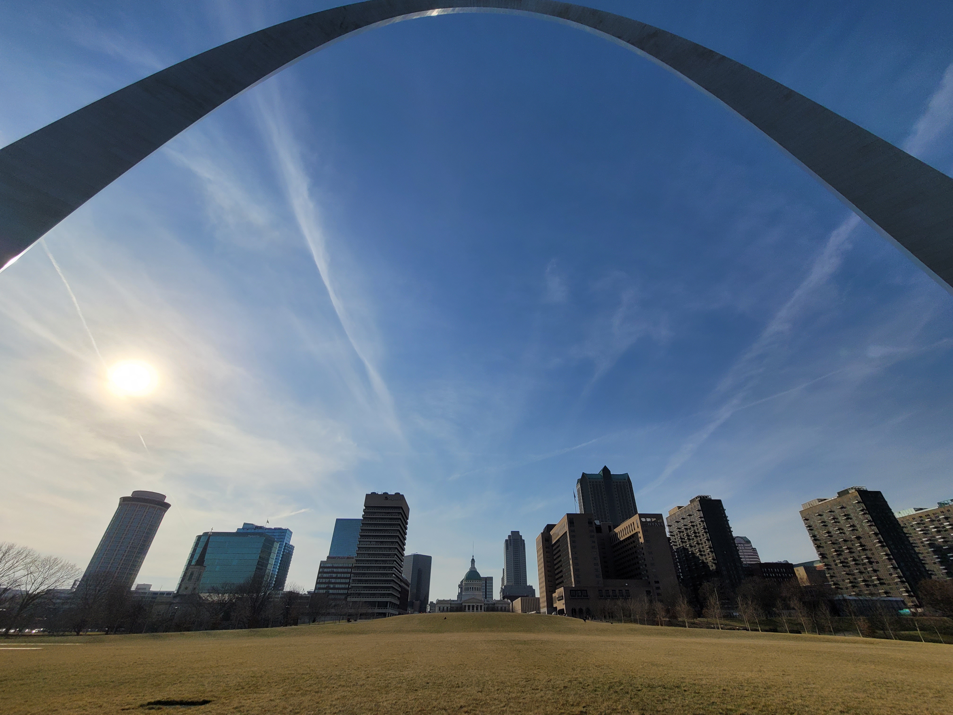 looking up at the curve of the Gateway Arch from below and the city buildings against a blue sky
