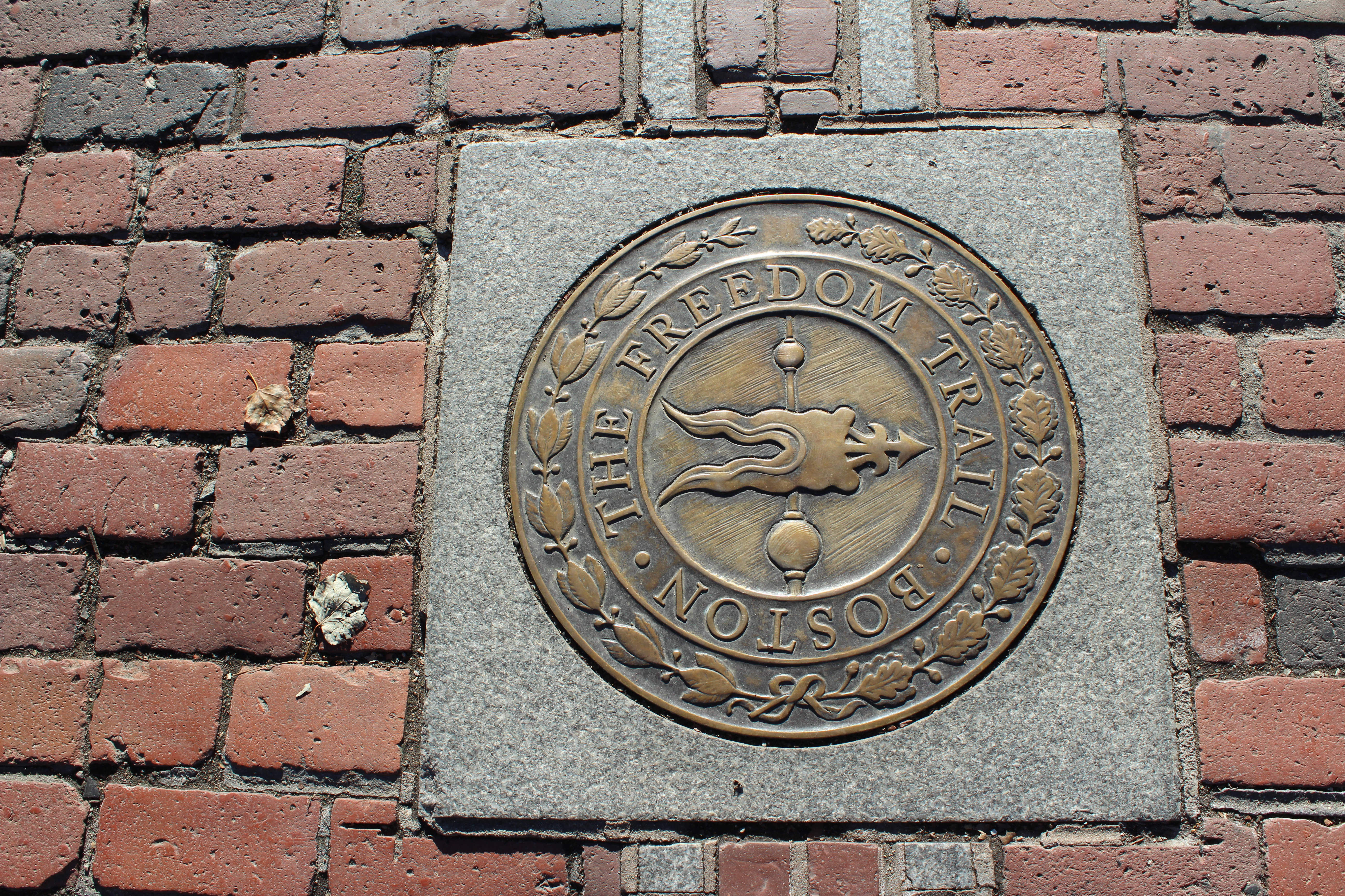 Photo looking down at a red brick sidewalk. In center is a bronze circular medallion