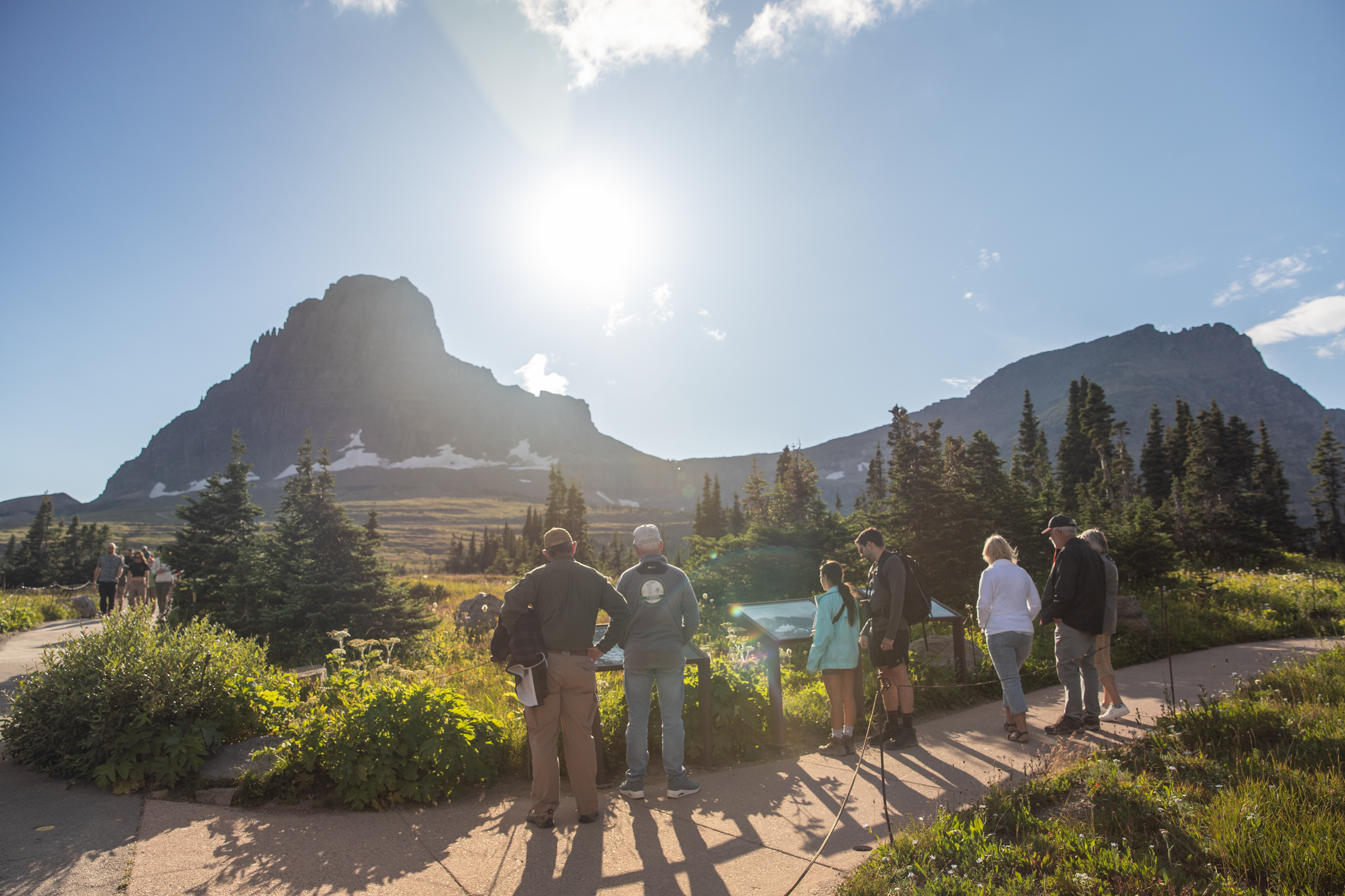 A group of people read exhibits with mountains in the background.