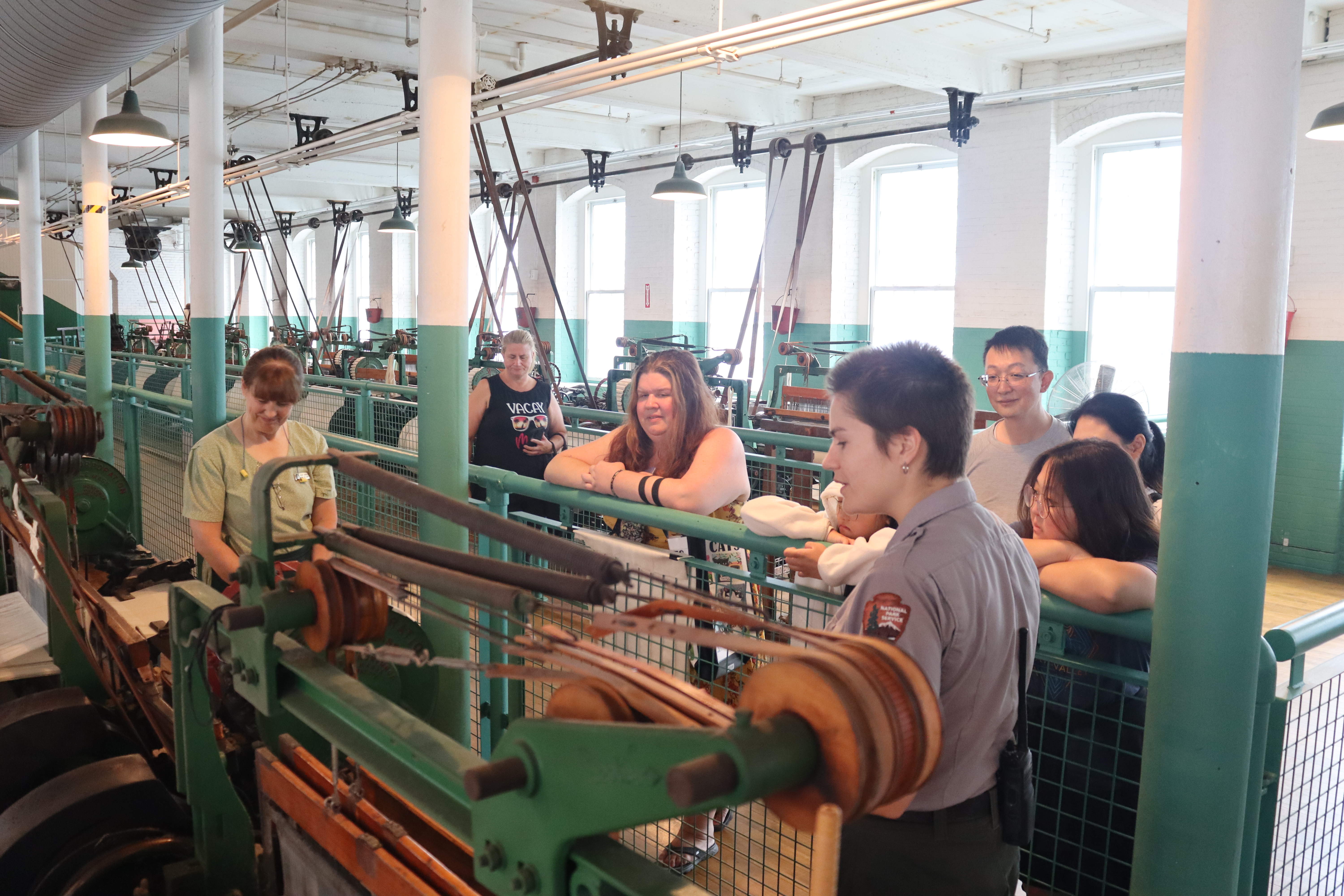 A ranger and weaver stand with a group of visitors looking at a historic power loom