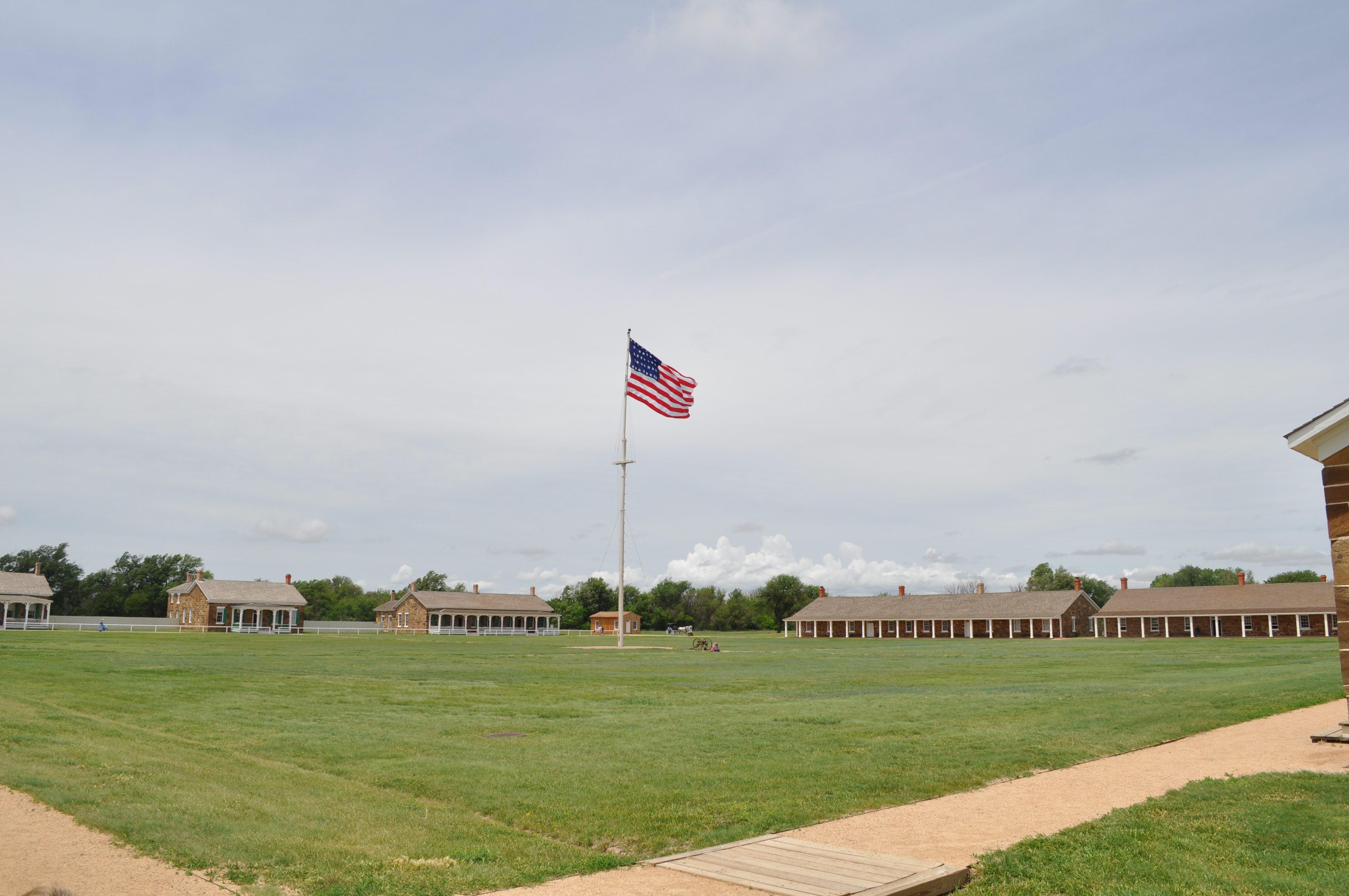 Large, square, grassy area with flagpole in the middle, sandstone block buildings surrounding it.