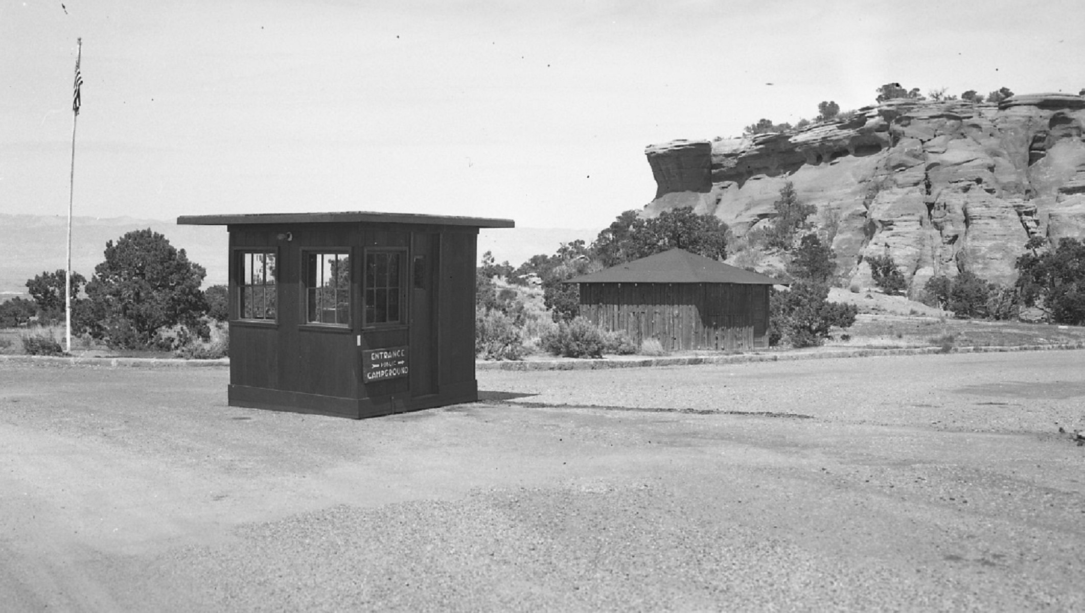 Entrance booth in middle of dirt road intersection, small building and rock outcrop in background.