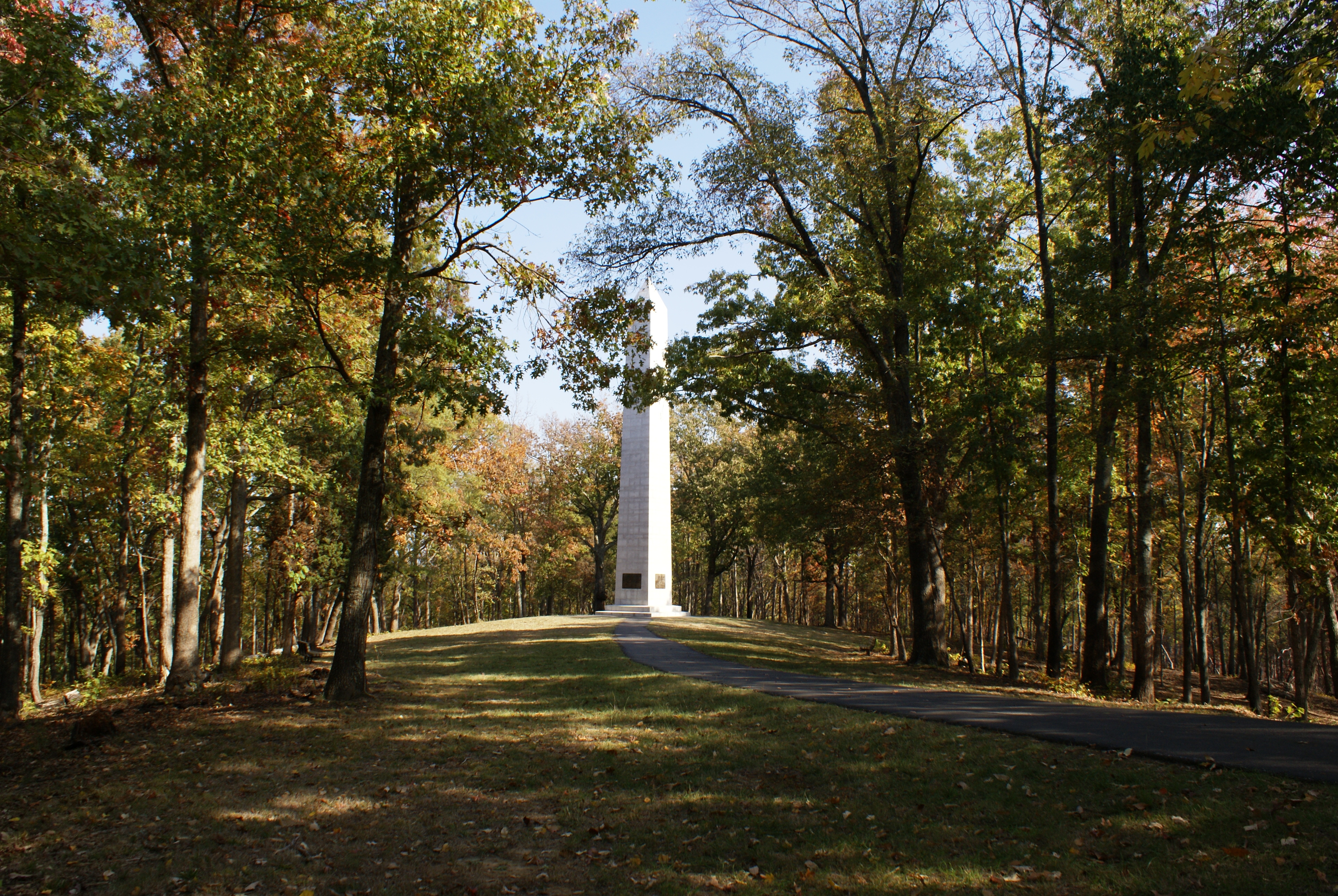 Paved path with trees on both sides, path leading to white obelisk
