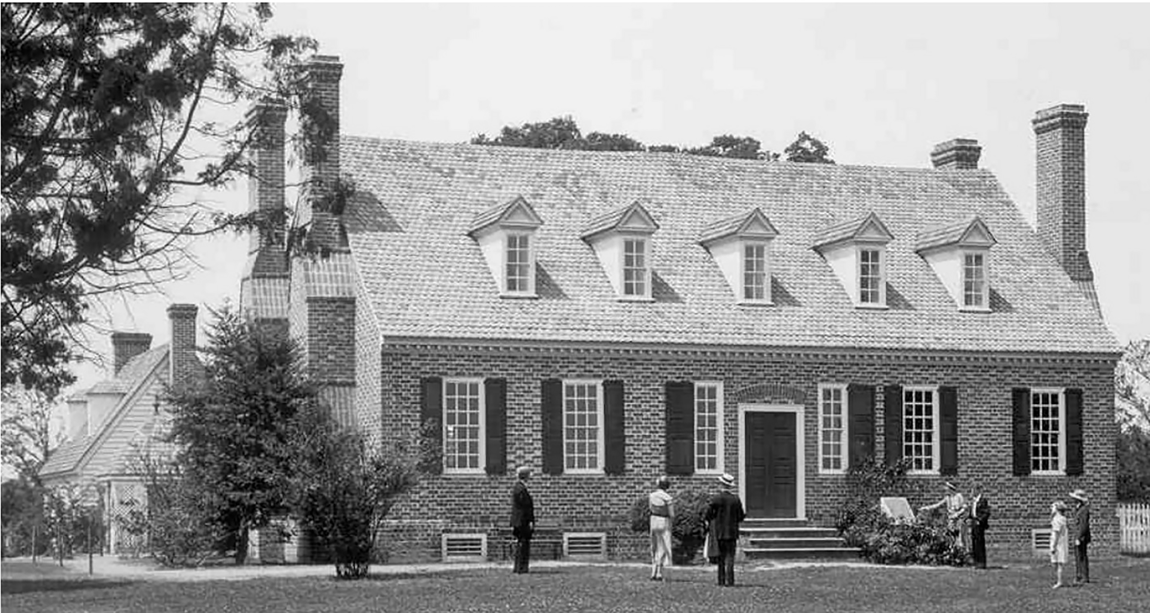 A black and white photo of a brick building with people walking up to the building.