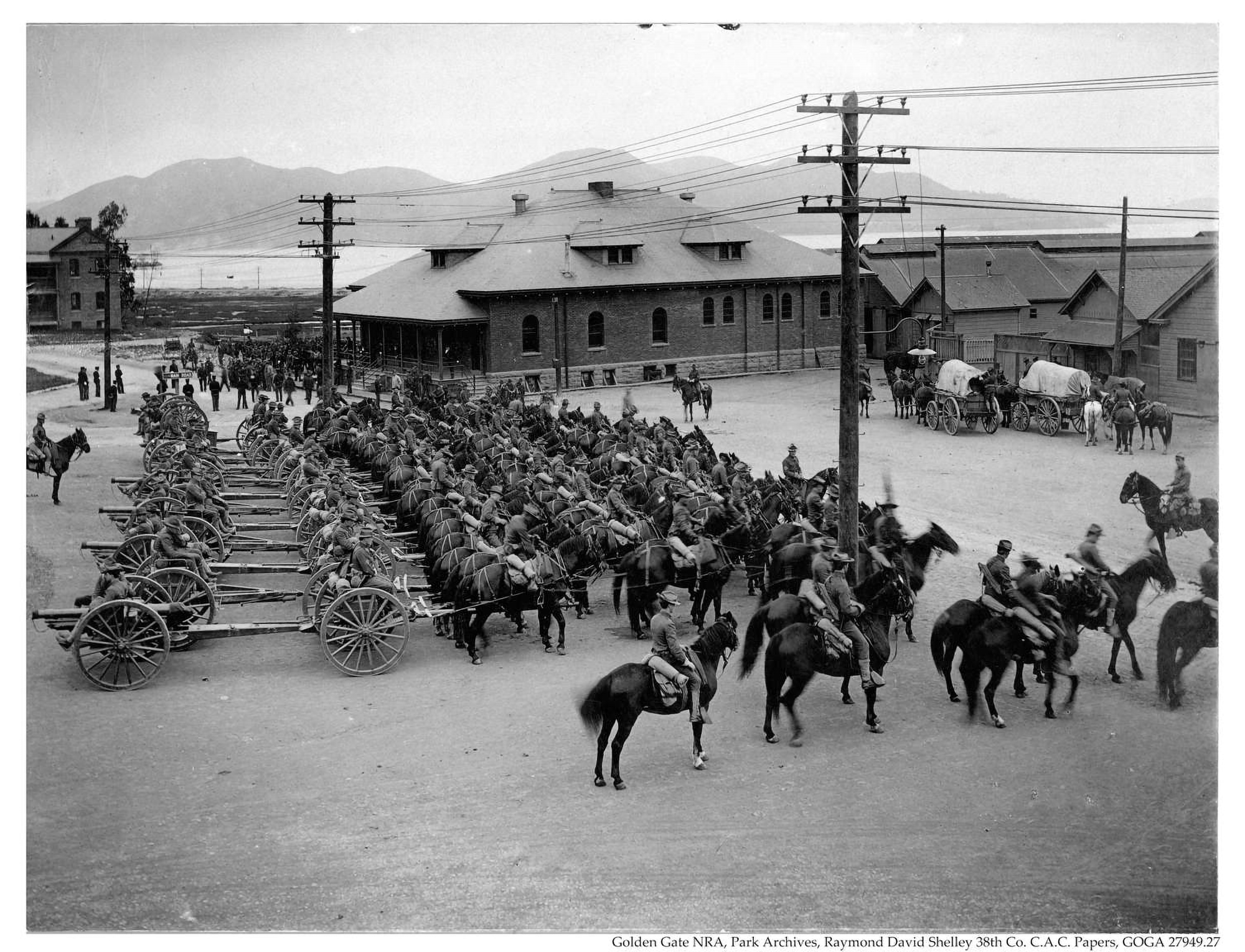 Black and white photo of soldiers preparing for travel, with horses and guns prepped.