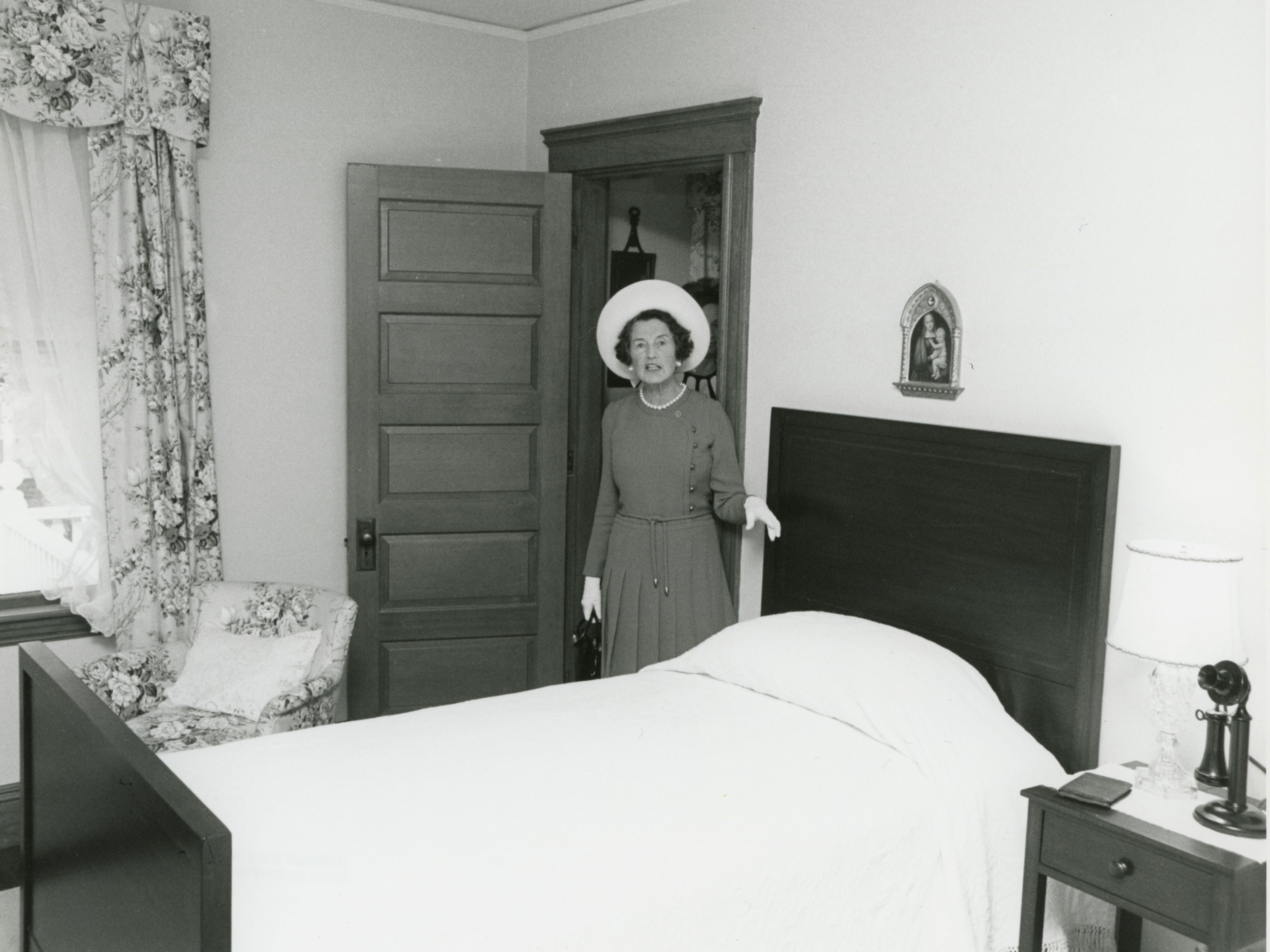 Woman in white hat standing next to twin bed