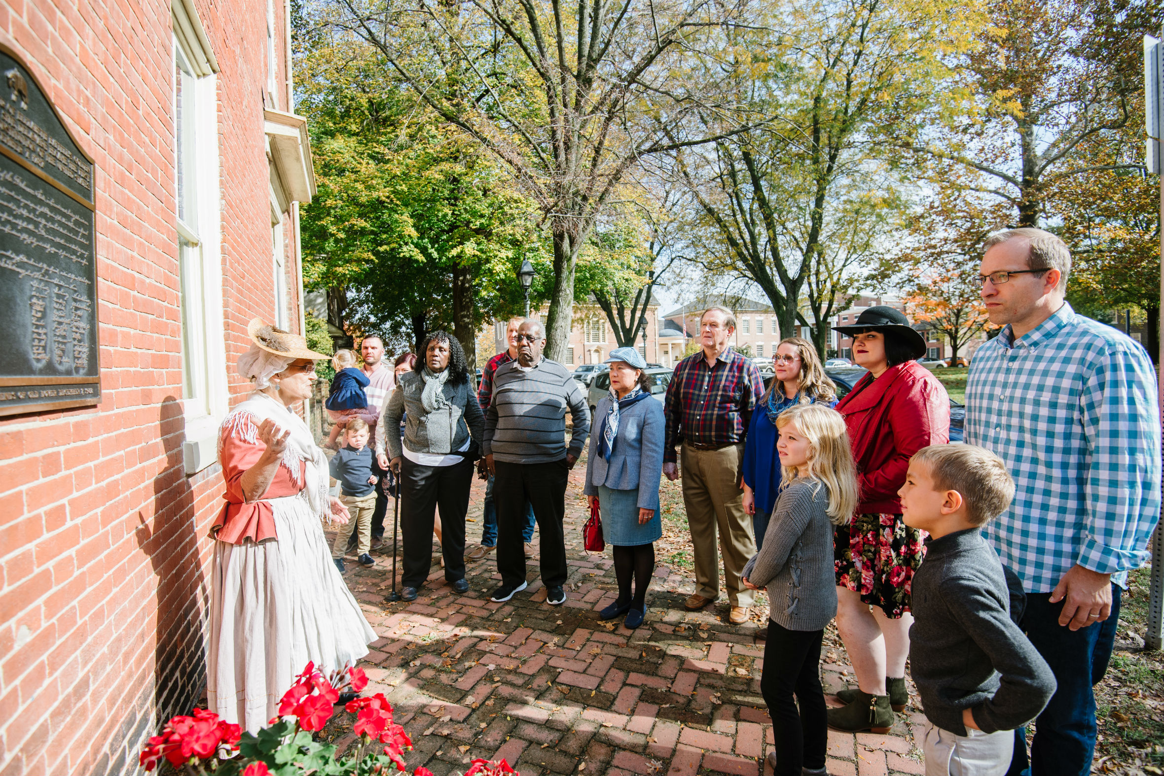 A group of people listen to a women in colonial clothing.