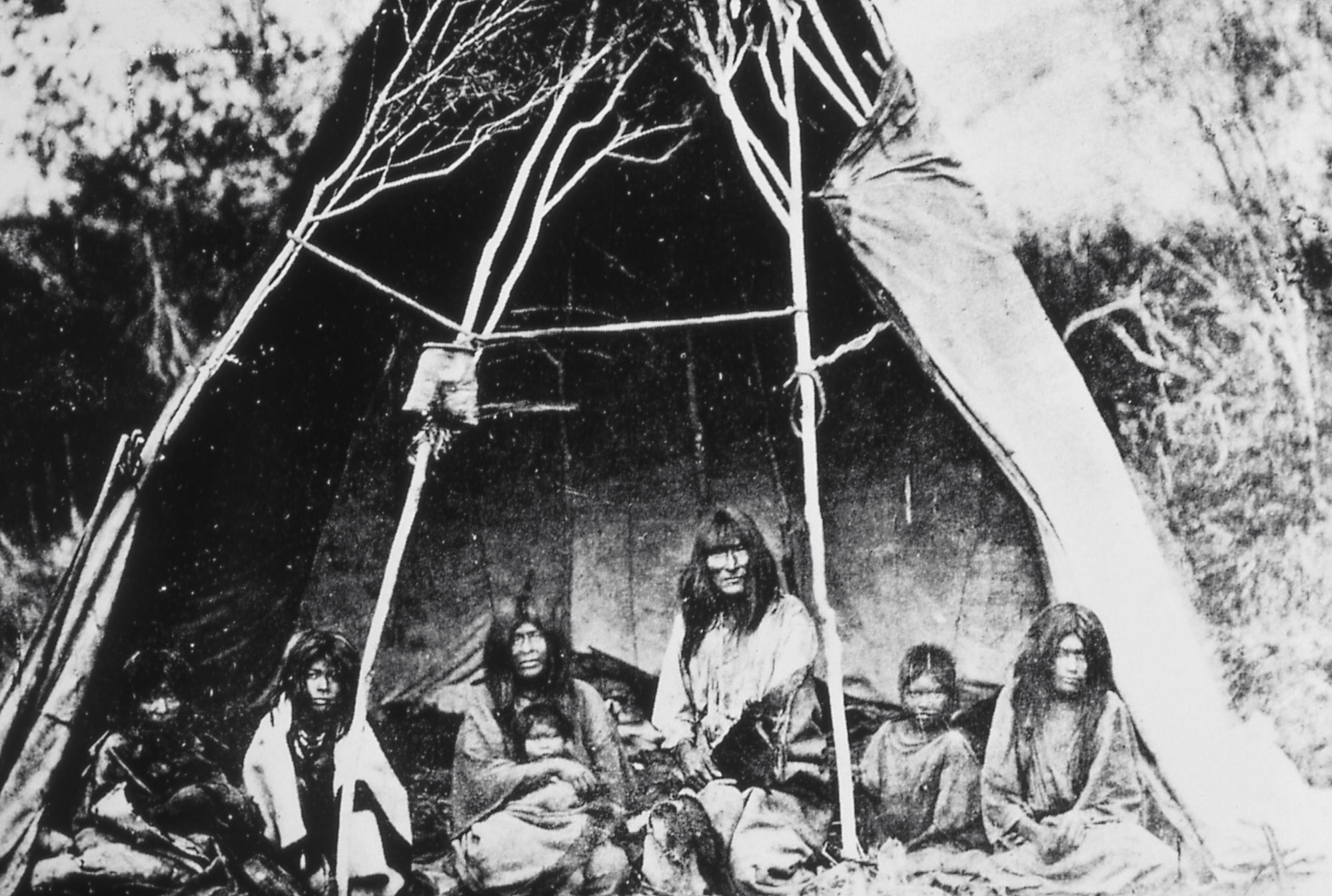 A group of people sitting inside a teepee structure.