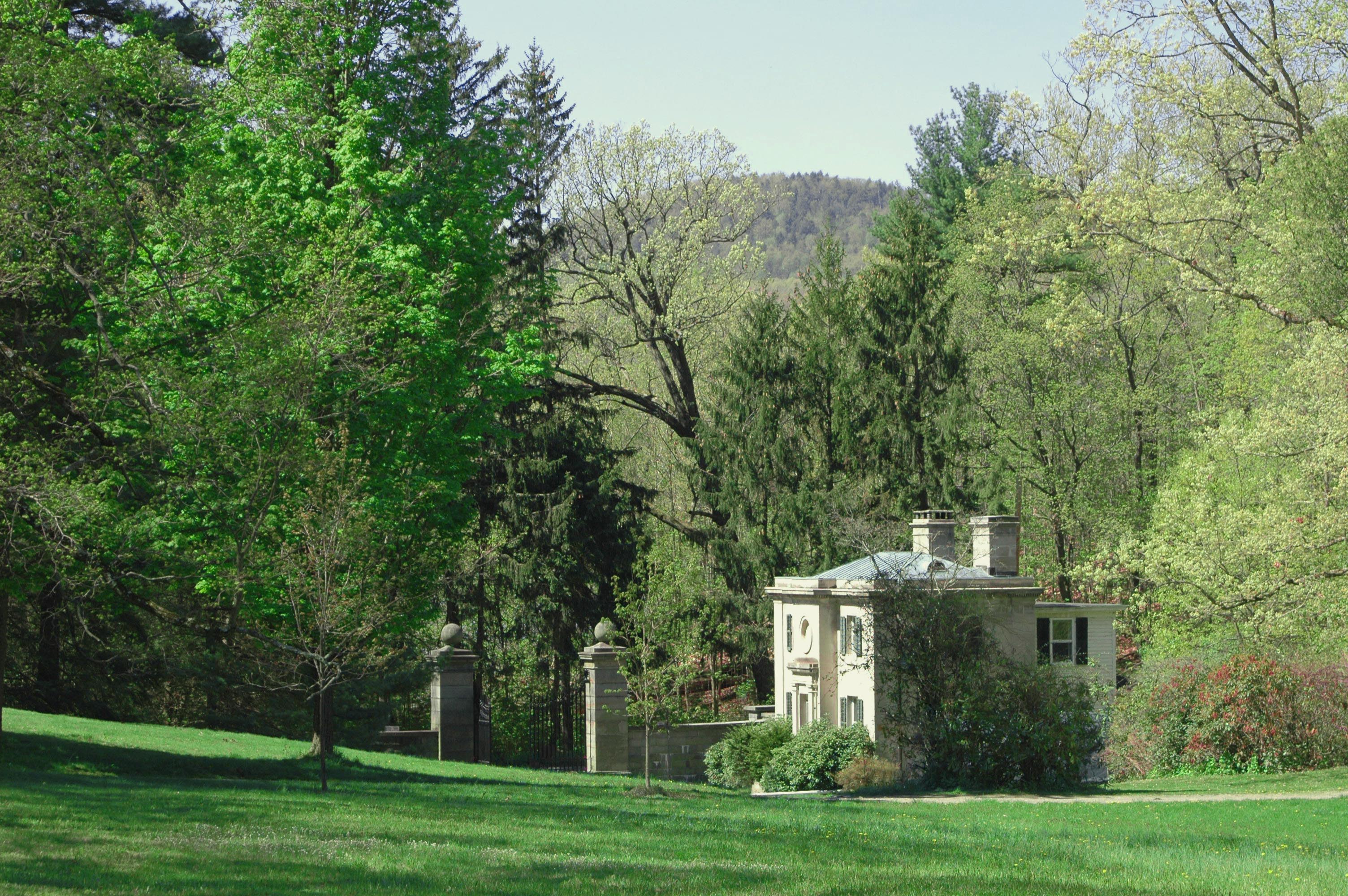 A small stone house with grand gate surrounded by lush lawn and trees.