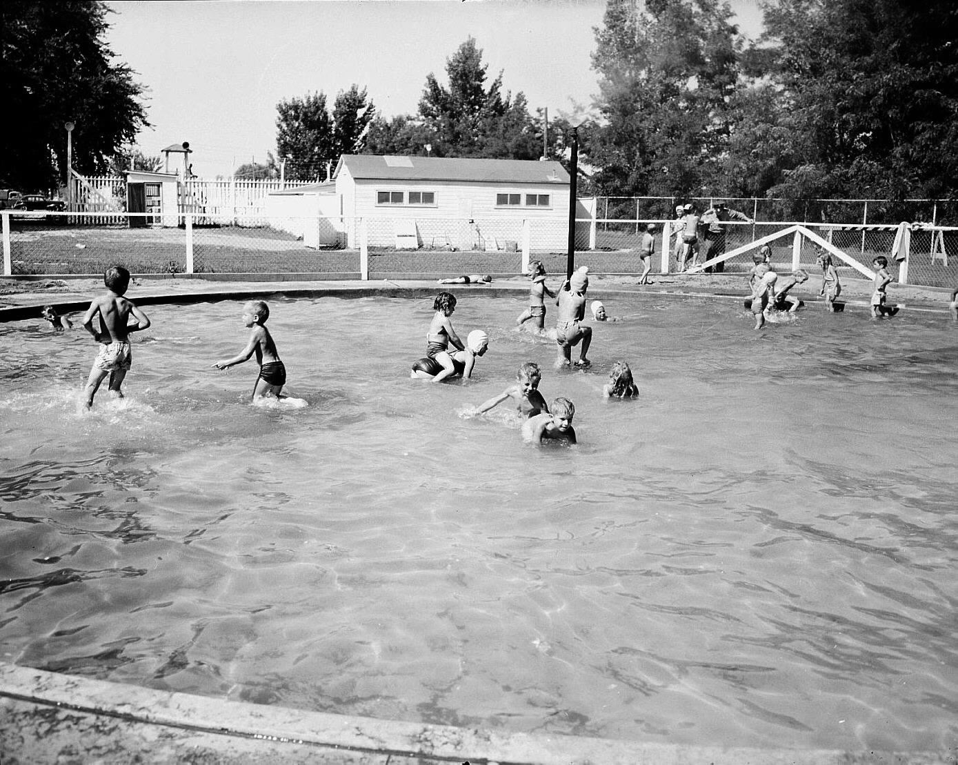 Black and white photograph of a group of children engaged in activities in a shallow wading pool