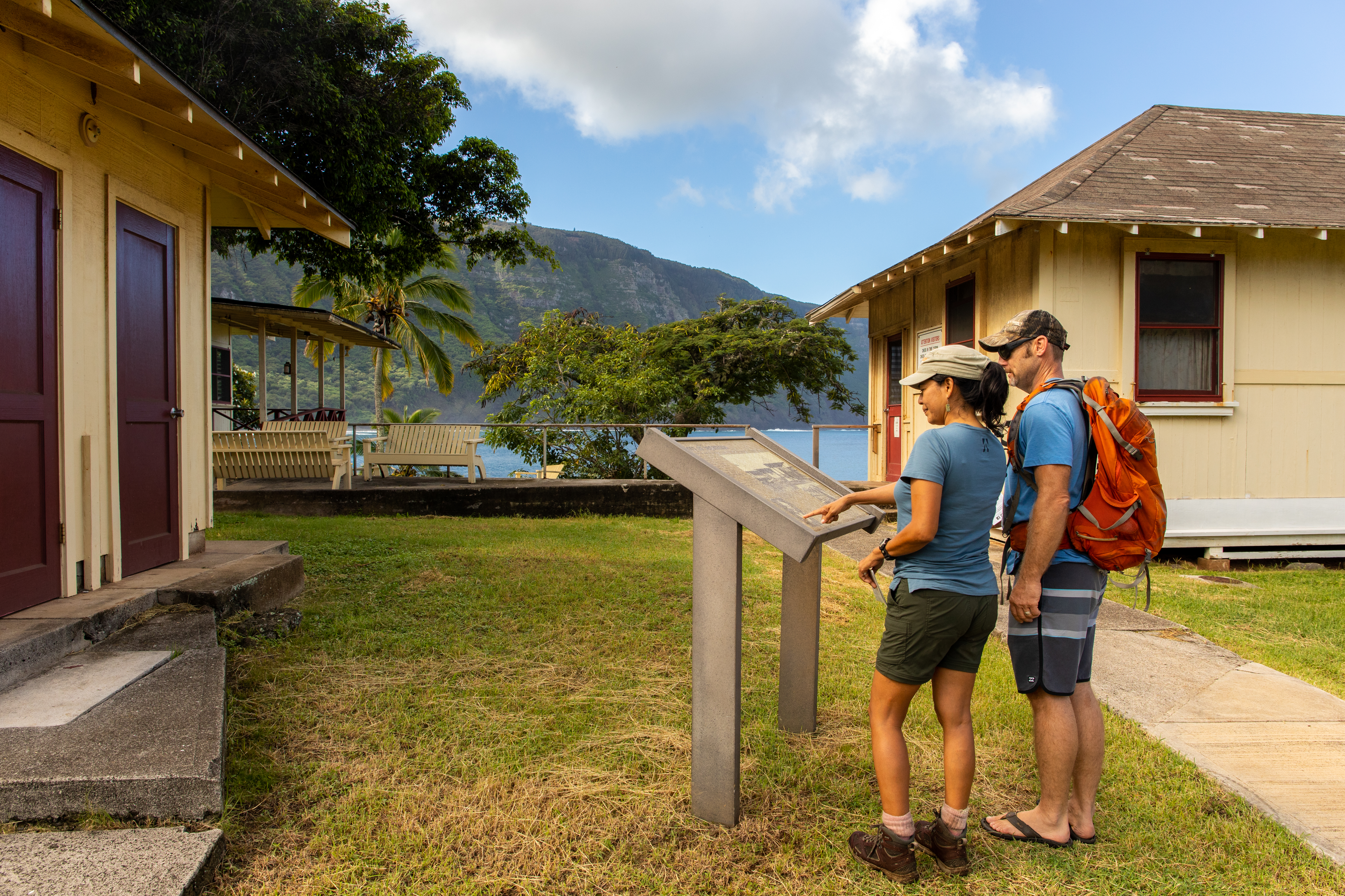 Two people looking at an information sign near buildings on the coast.