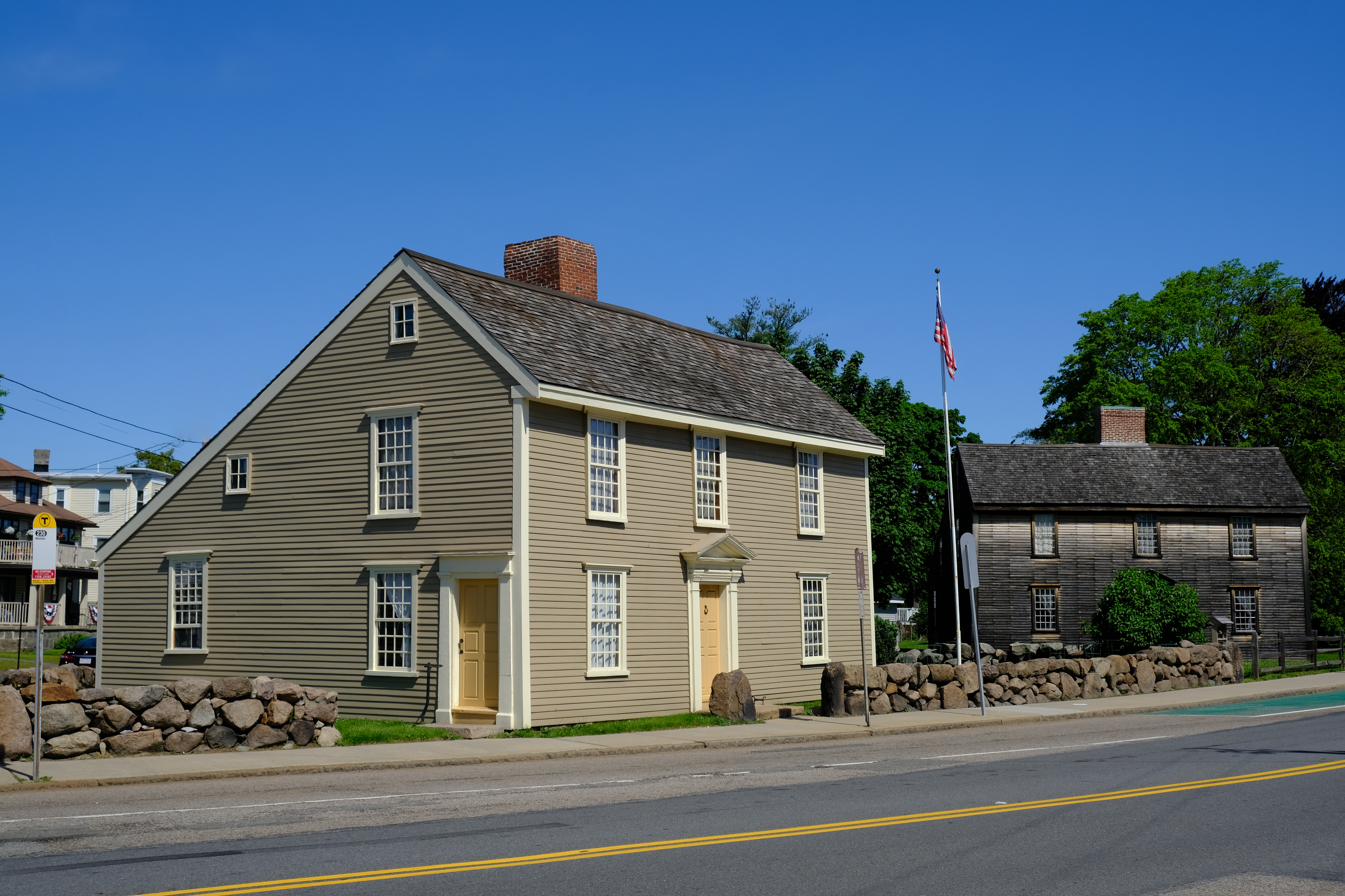 Two New England "salt-box" style homes sit next to each other near a road.