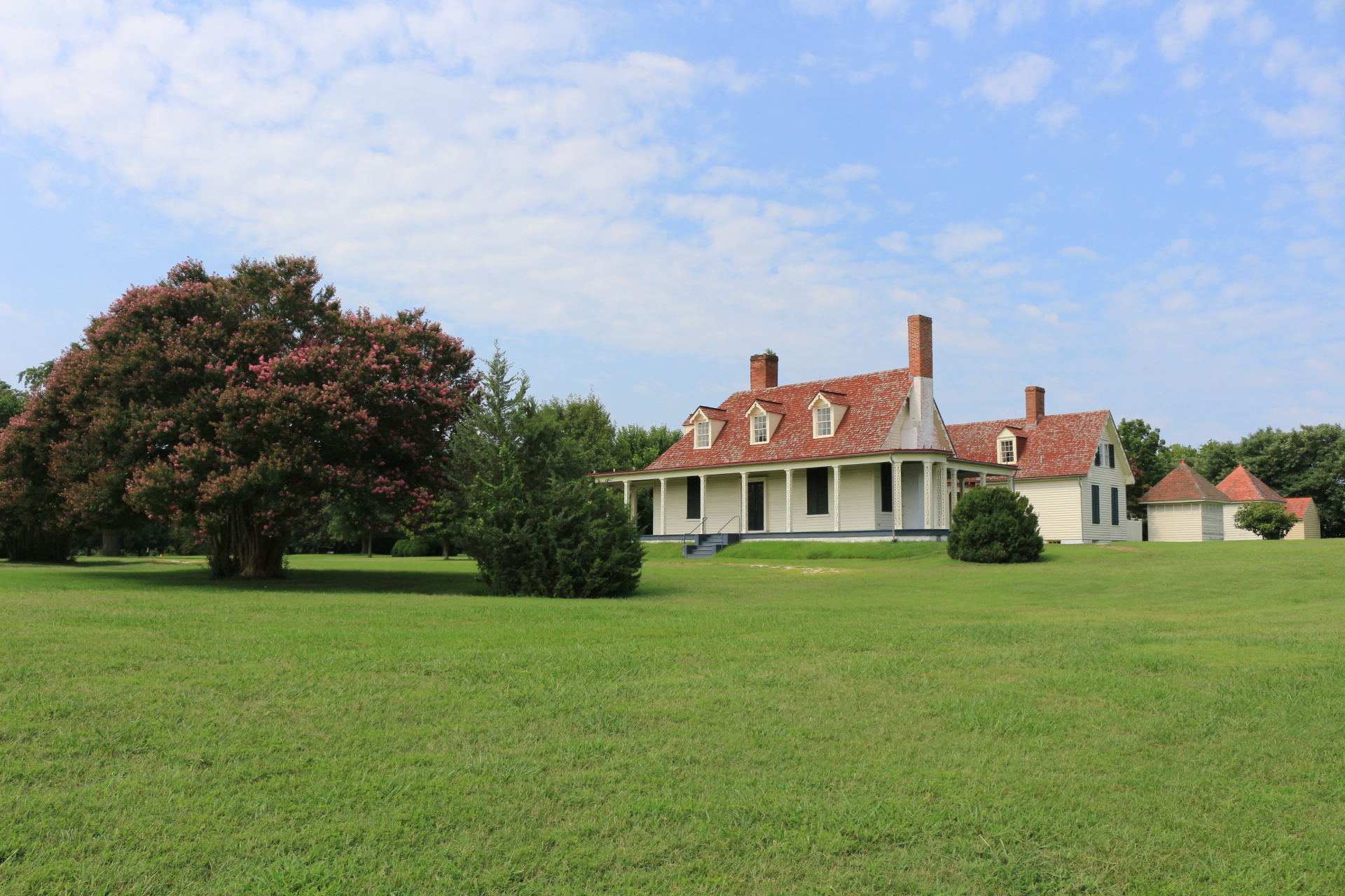white house with red roof, two smaller buildings background with green grass and blue sky