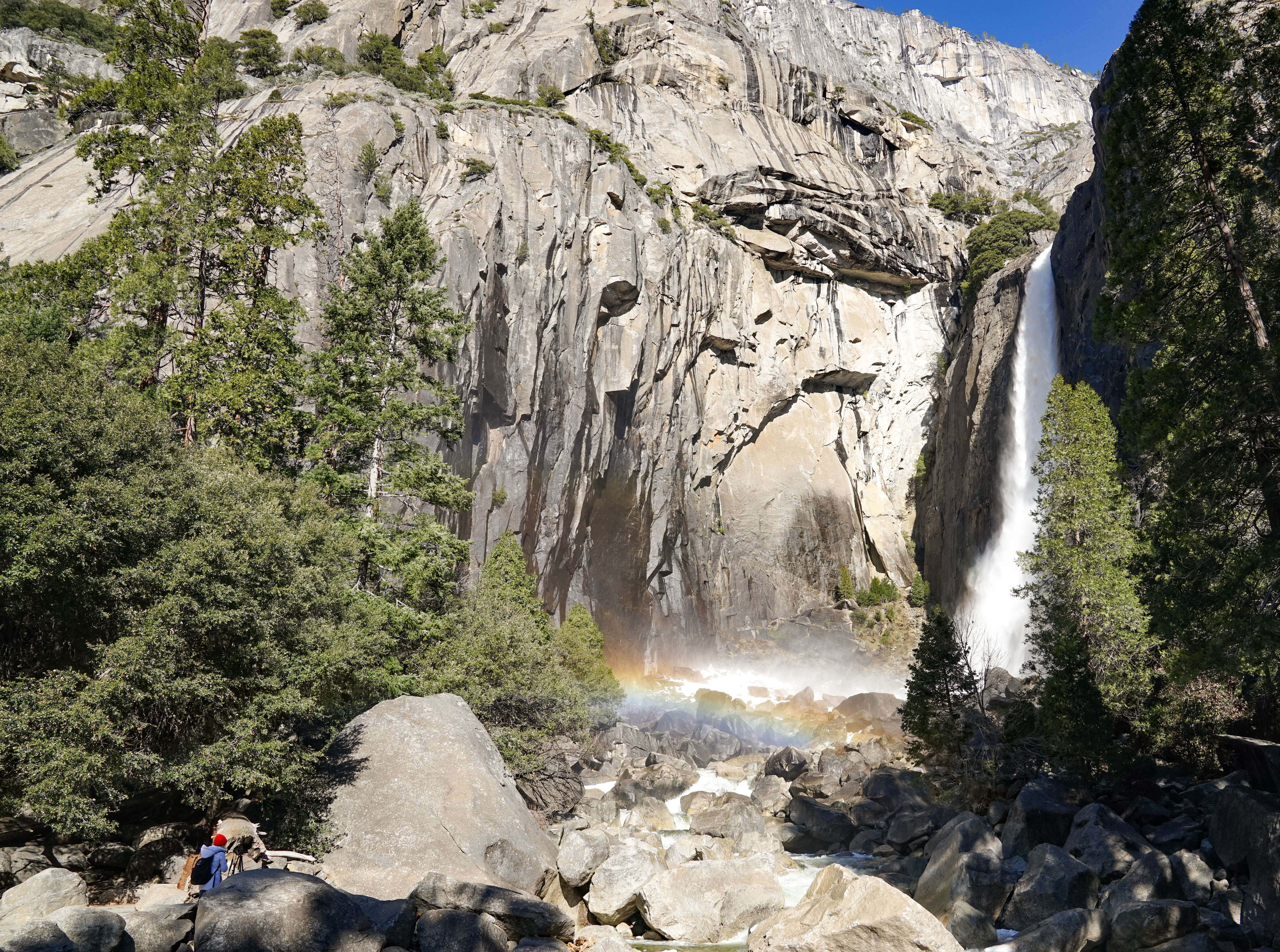 A rainbow forms in the mist at the bottom of a waterfall