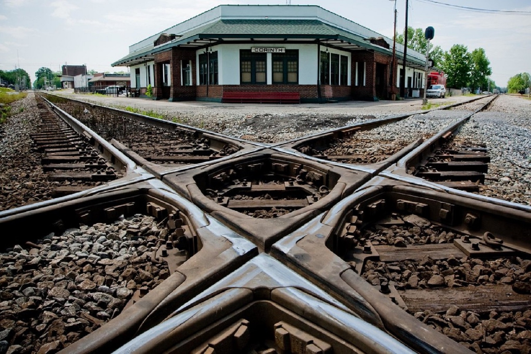 Image of two rail lines crossing with a white and green building in background.