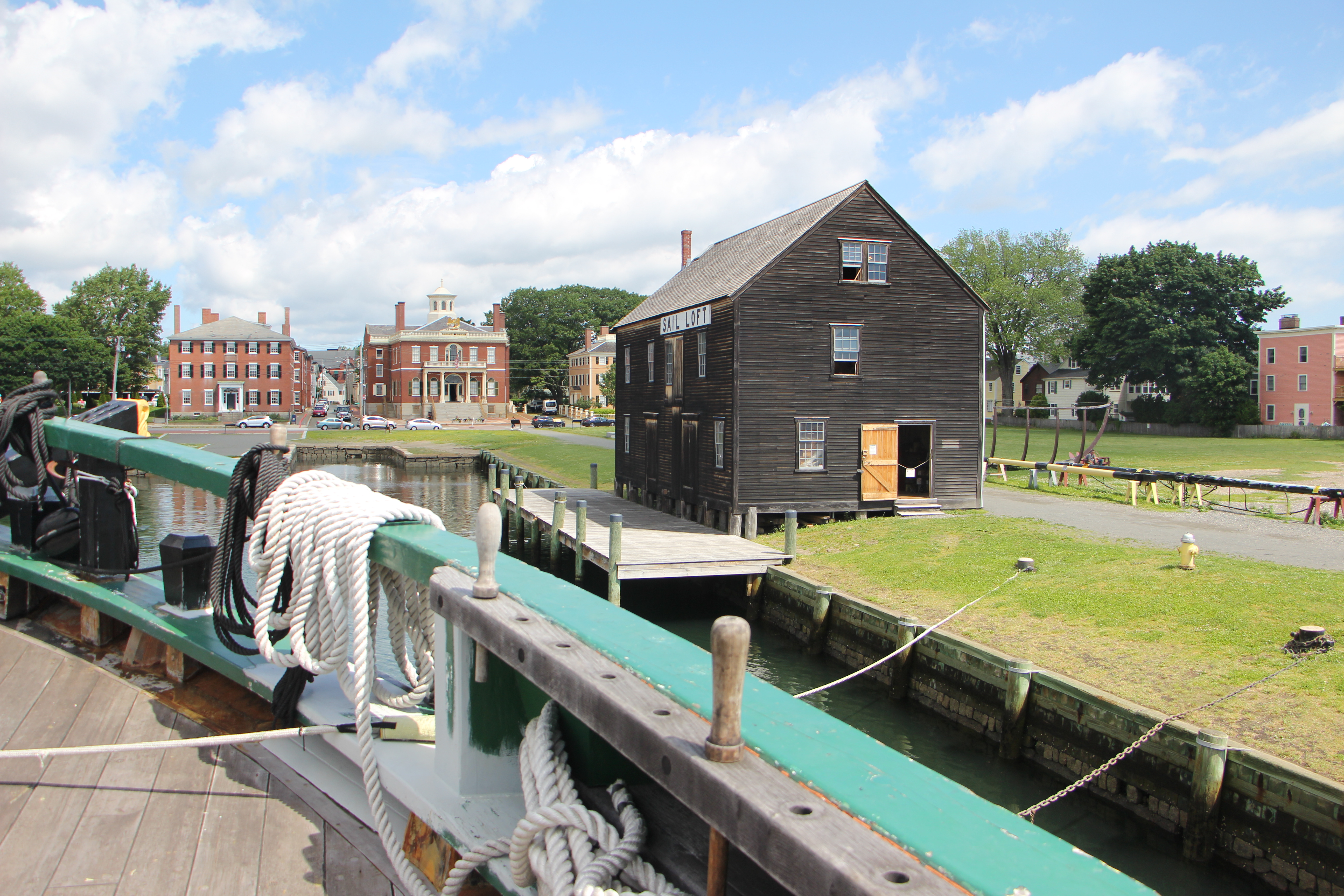 view from large sailing vessel of wood warehouse next to dock and multi-story brick buildings
