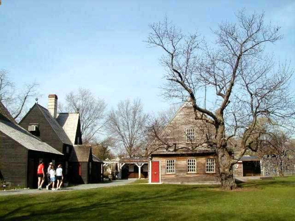 three people follow a path around the back of a house to a wood-sided museum with bright red door