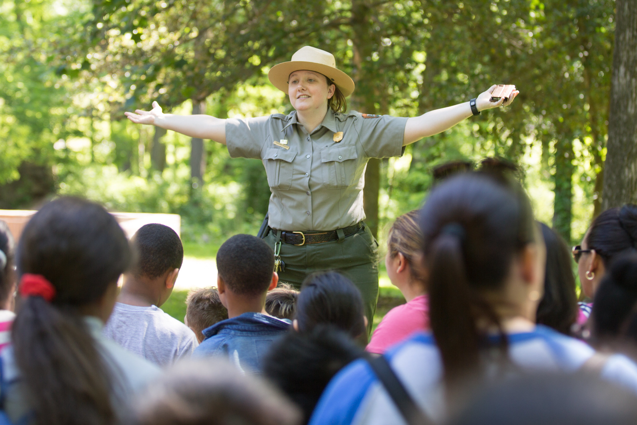 Ranger with her arms out speaking to a large group of young students.