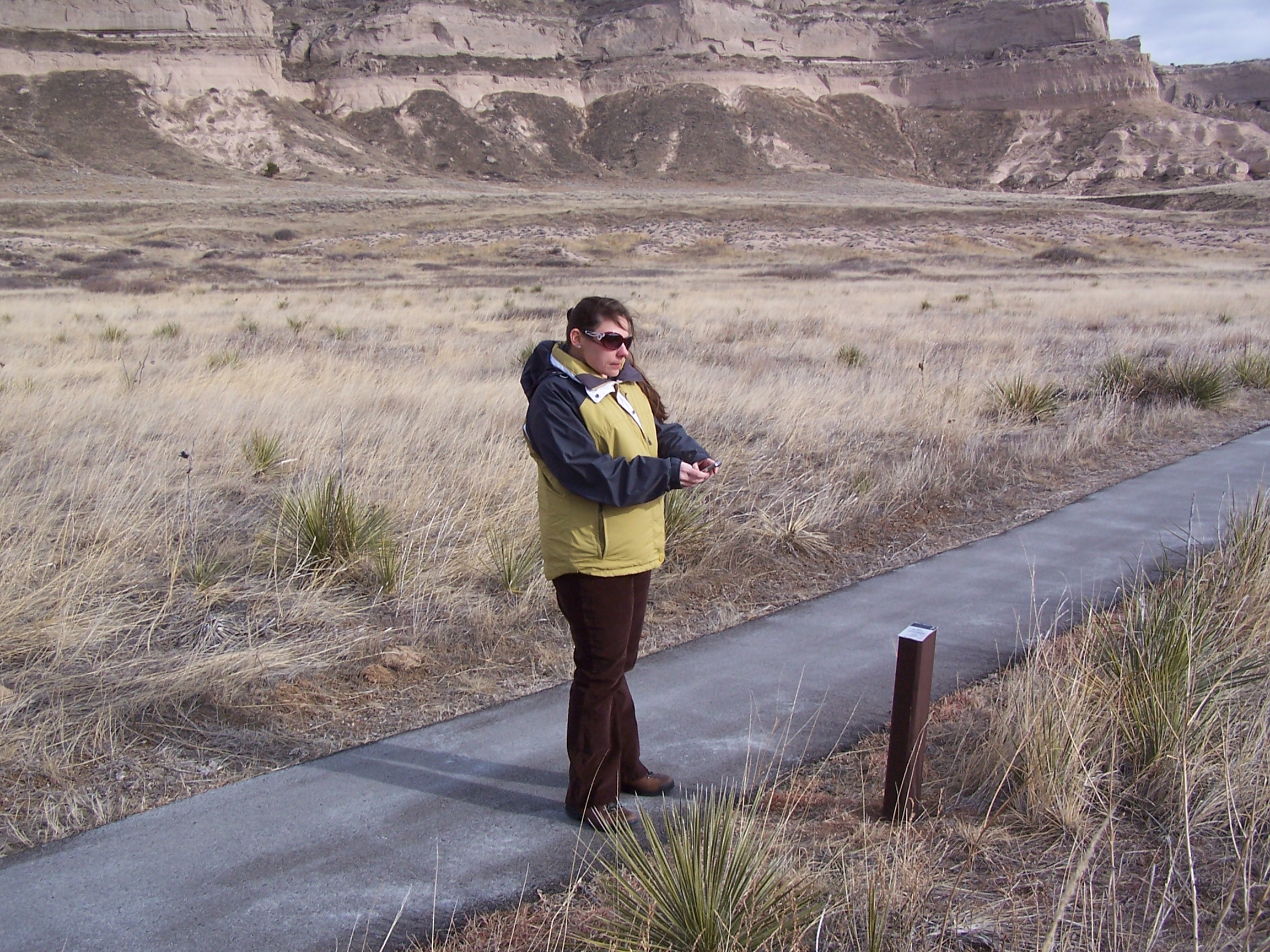 A woman stands on a paved trail and uses her smart phone to listen to an audio tour.