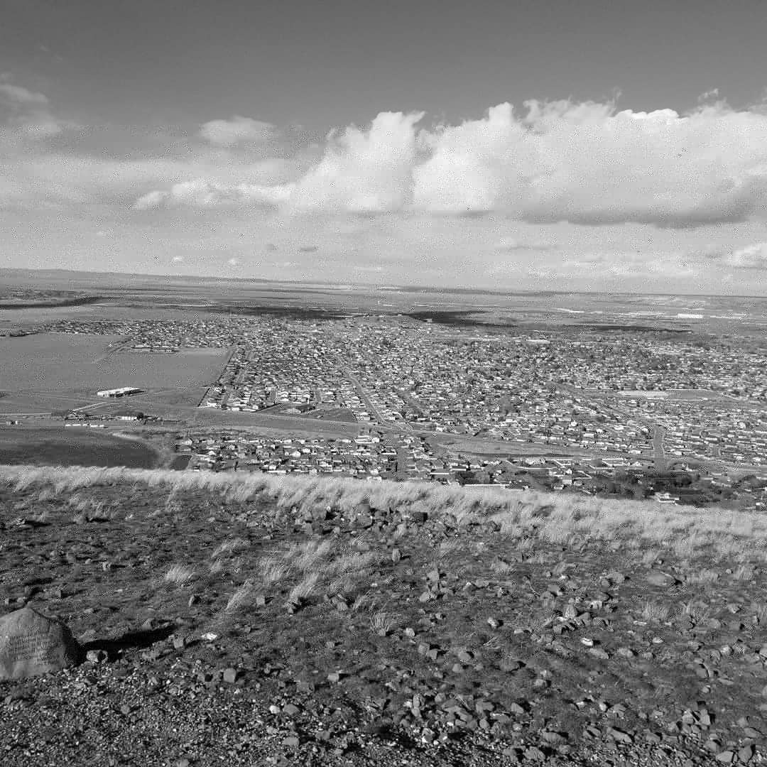 Black and white photograph of a cityscape spreading out below as viewed from a mountain's summit.