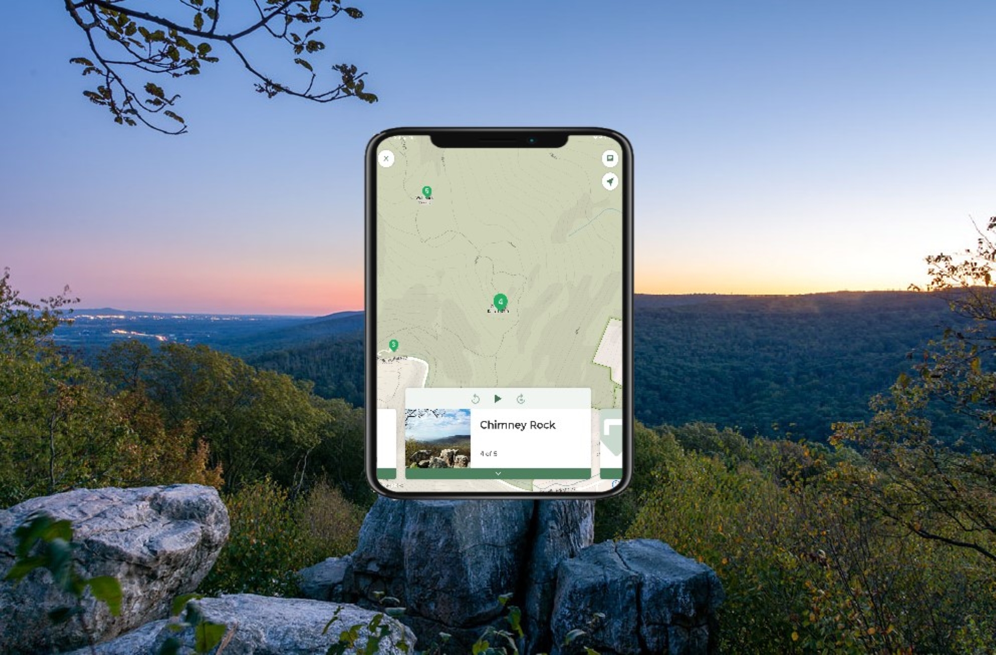 A large rocky outcrop looking over a mountain ridge at sunset with a phone over the image.