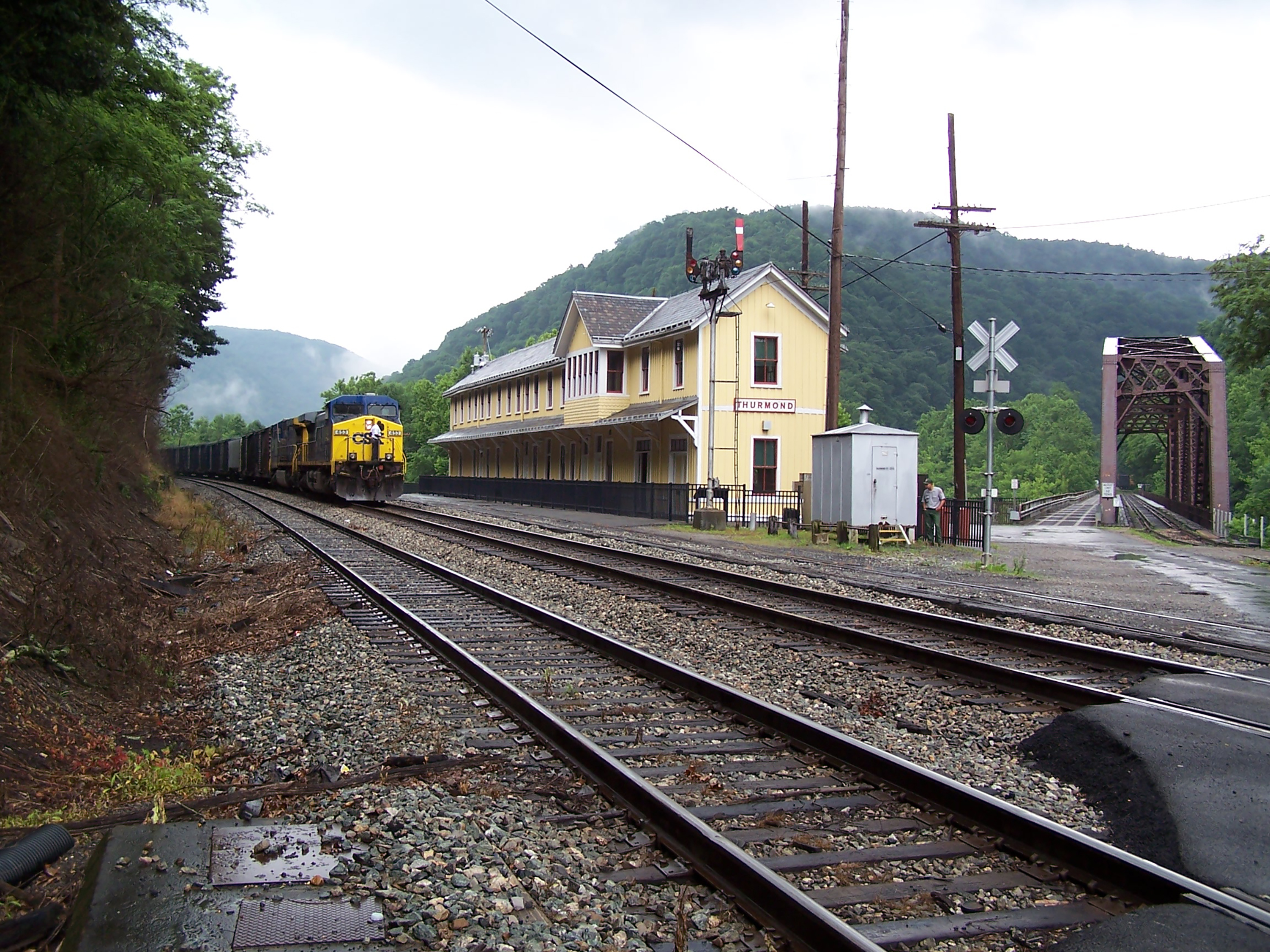 A yellow long building next to railroad tracks with a blue and yellow train on them