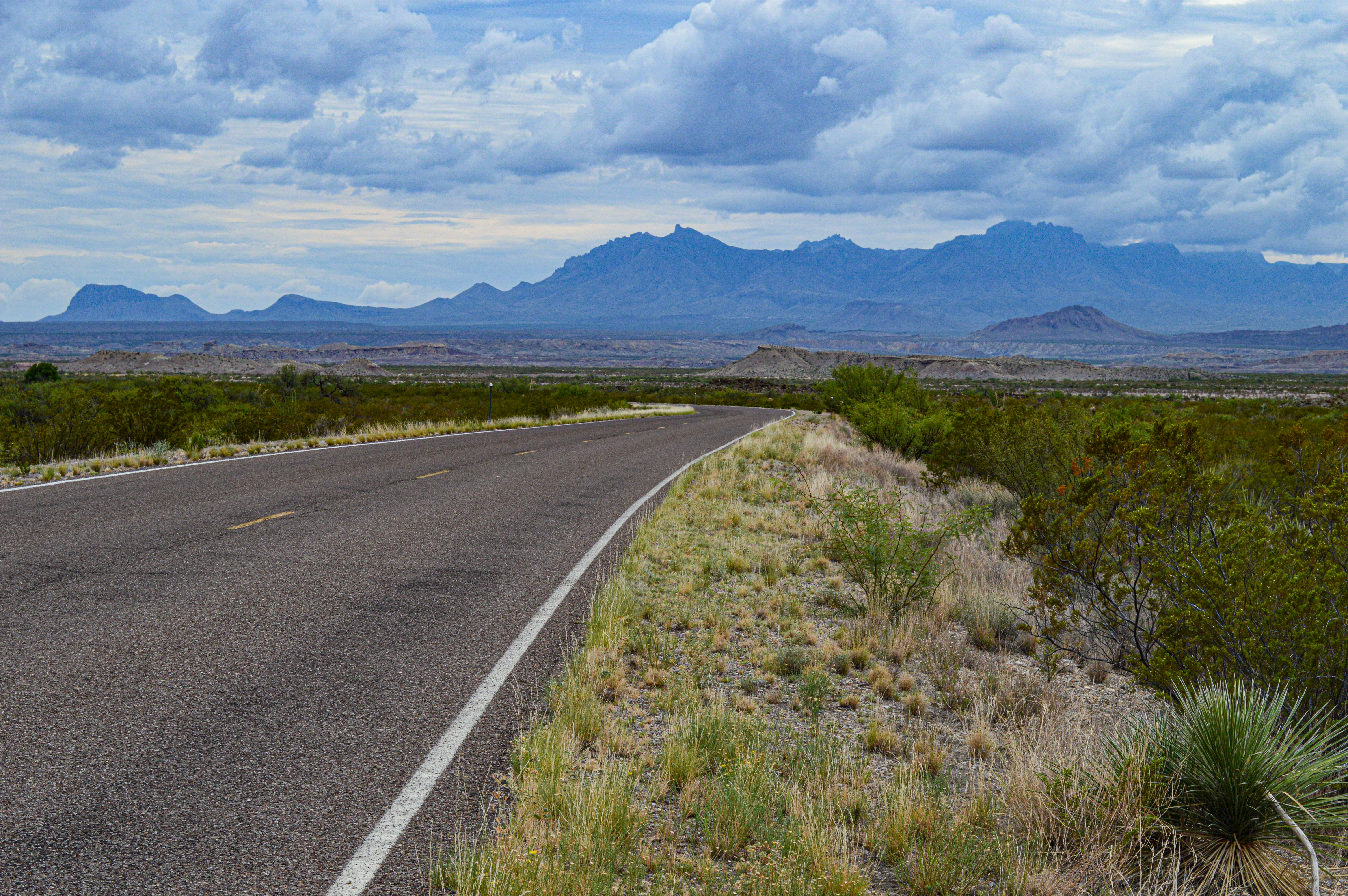 A paved road heads in a straight line through the desert towards a distant line of mountains.