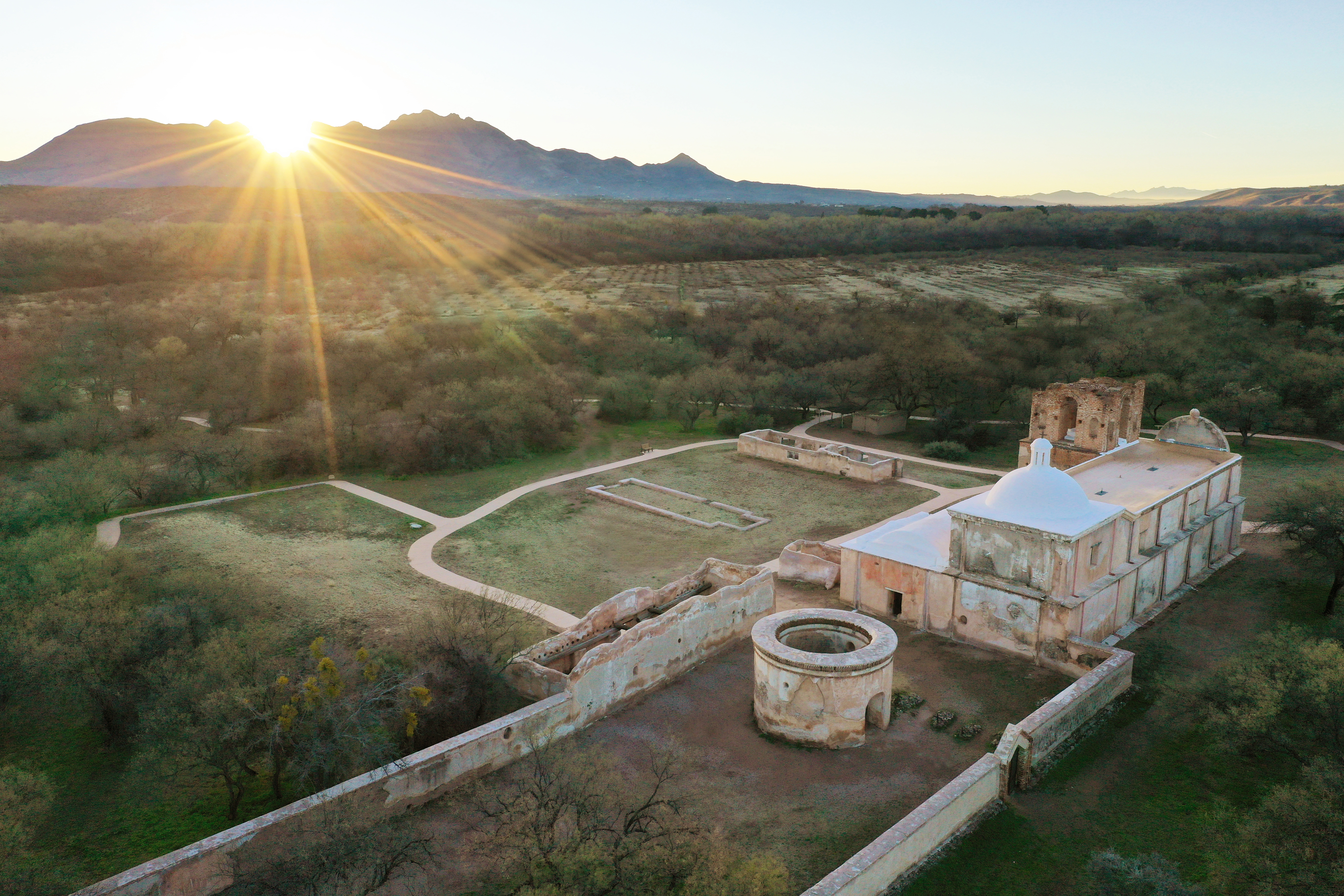aerial photo of mission grounds with sunburst coming from behind the mountains