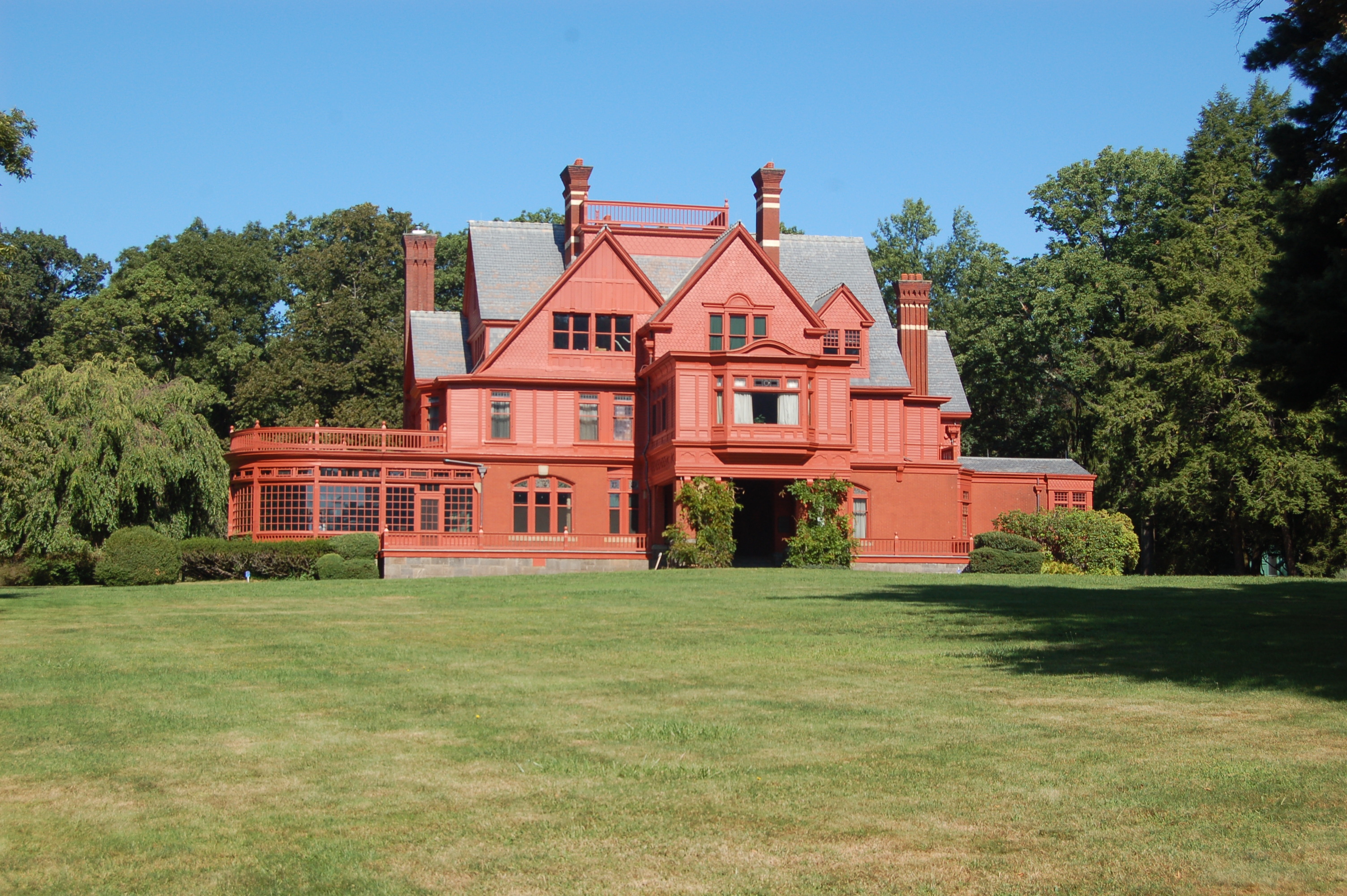 Red, brick colored Victorian era building, surrounded by sky, trees and grass.