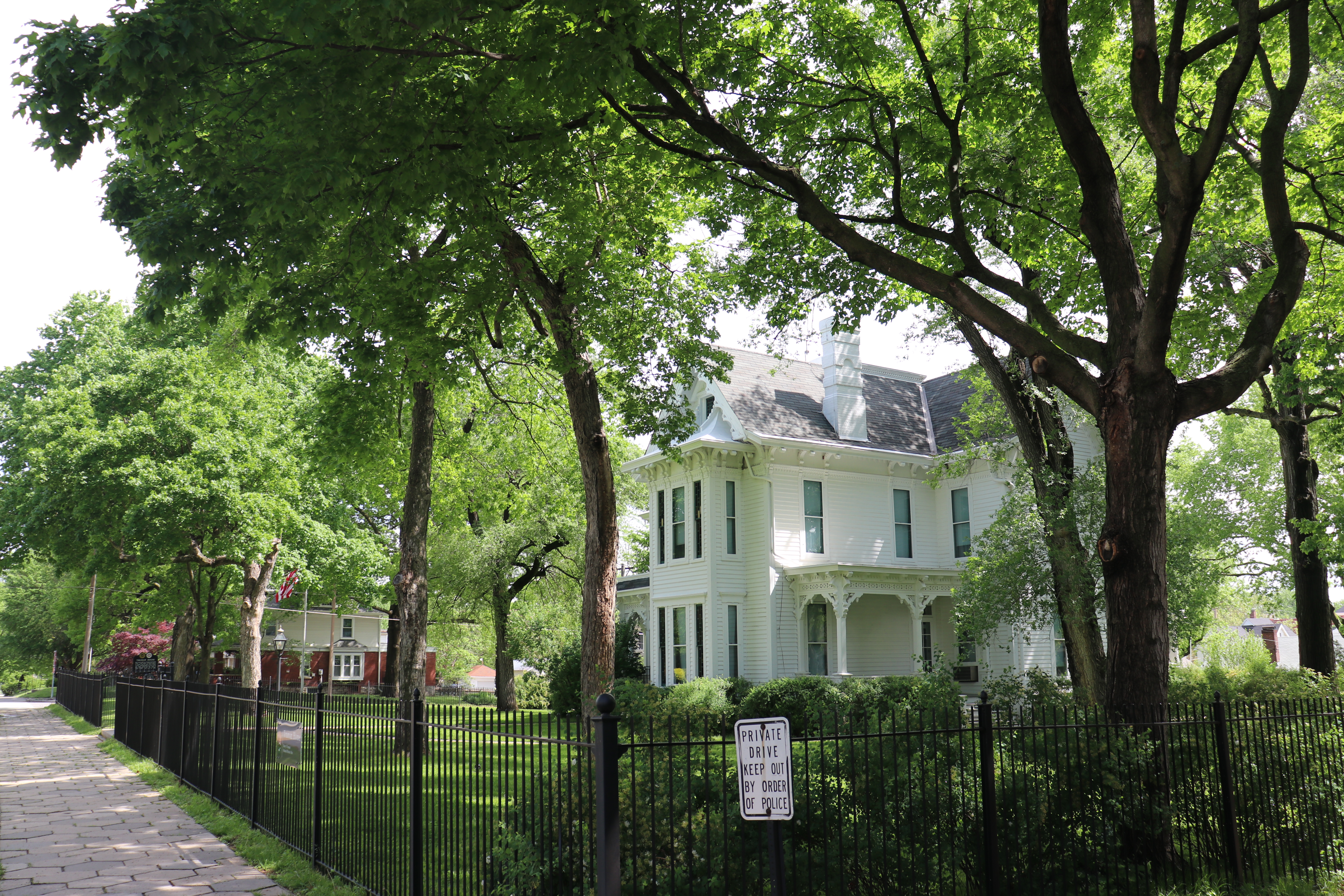 In the foreground a black fence, shrubs, and trees and in the background, the white Truman home.