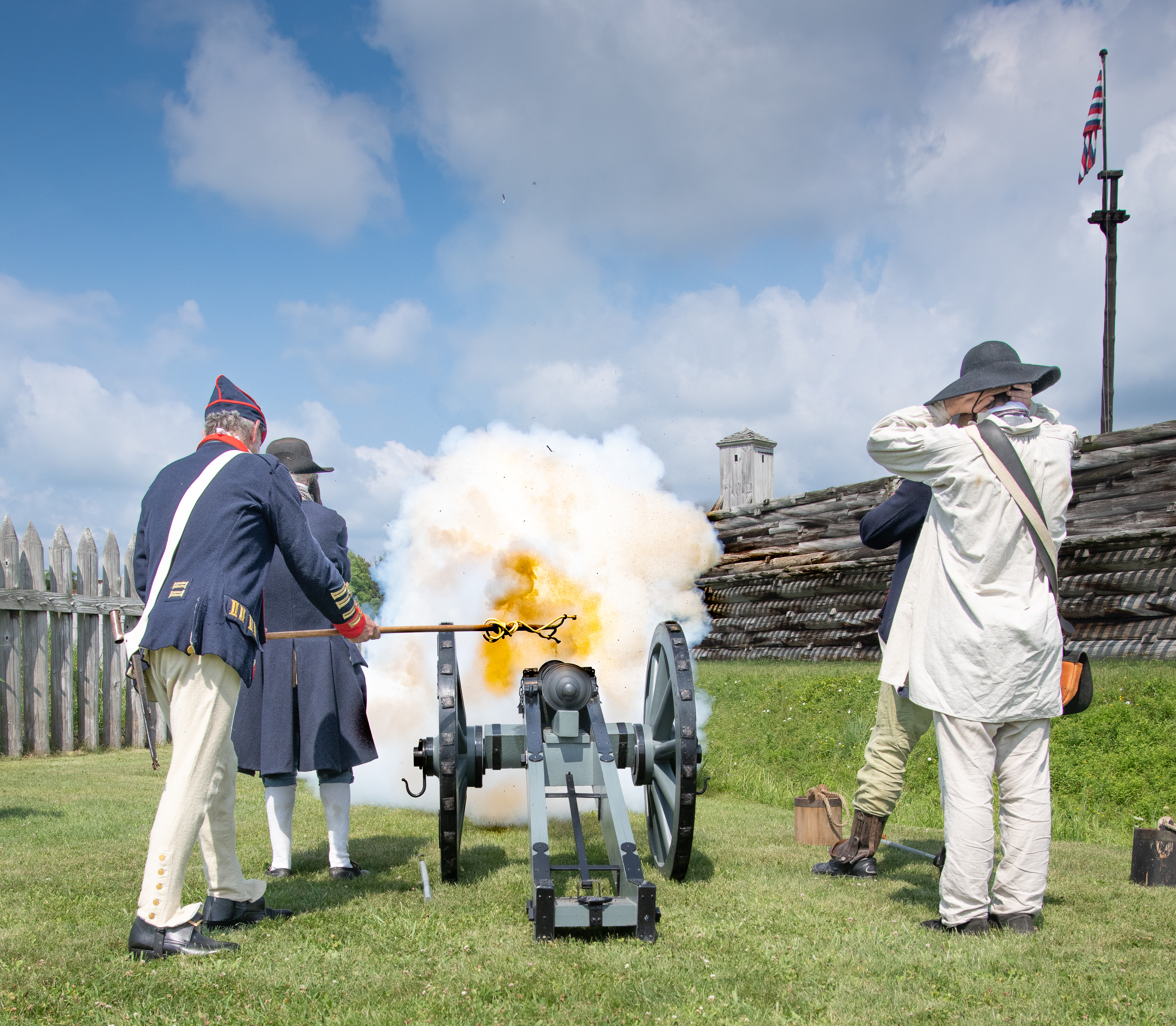 A view of a cannon crew from behind. They are actively firing. Smoke billows around them.
