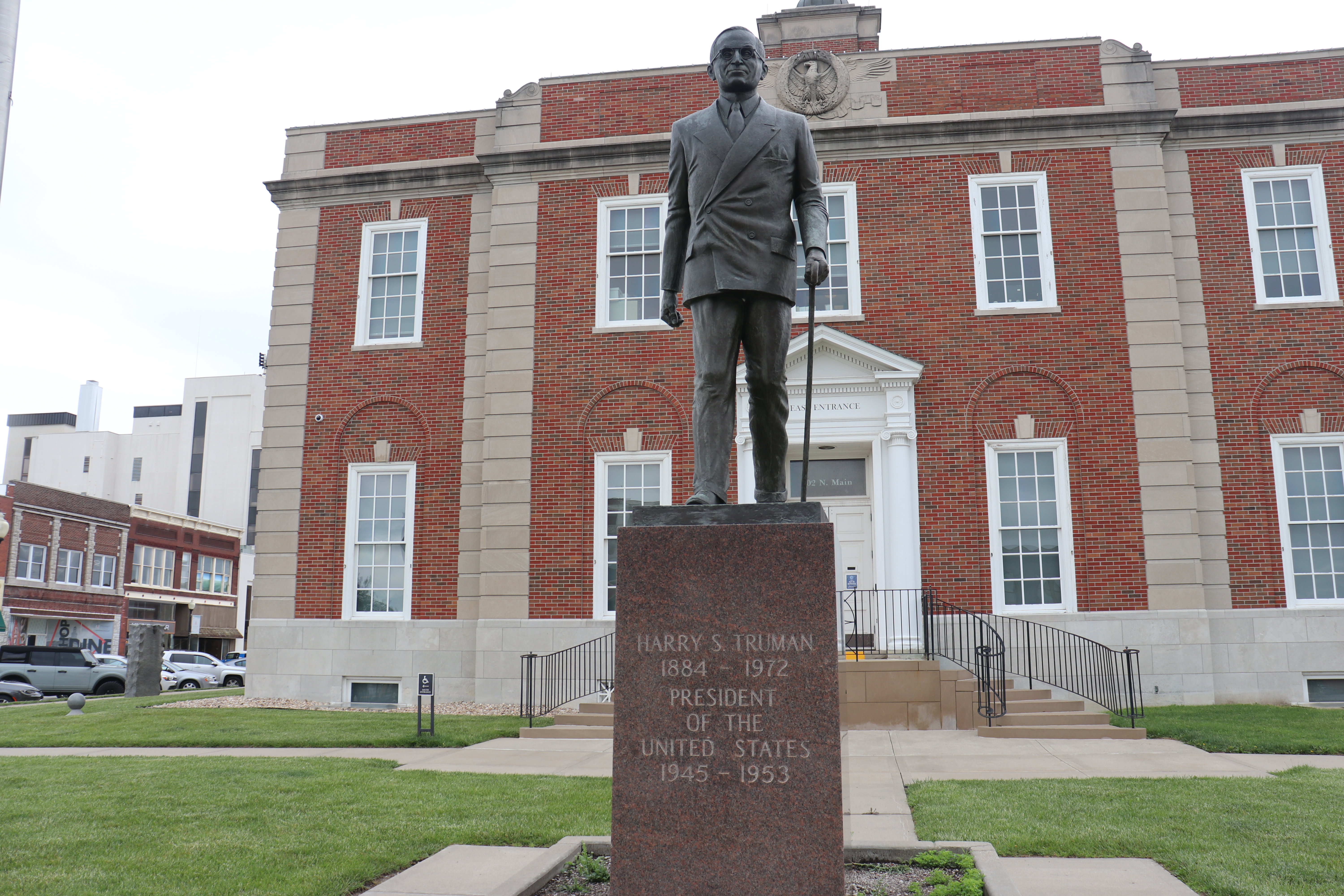A statue of Harry S Truman in front of the two story brick courthouse.