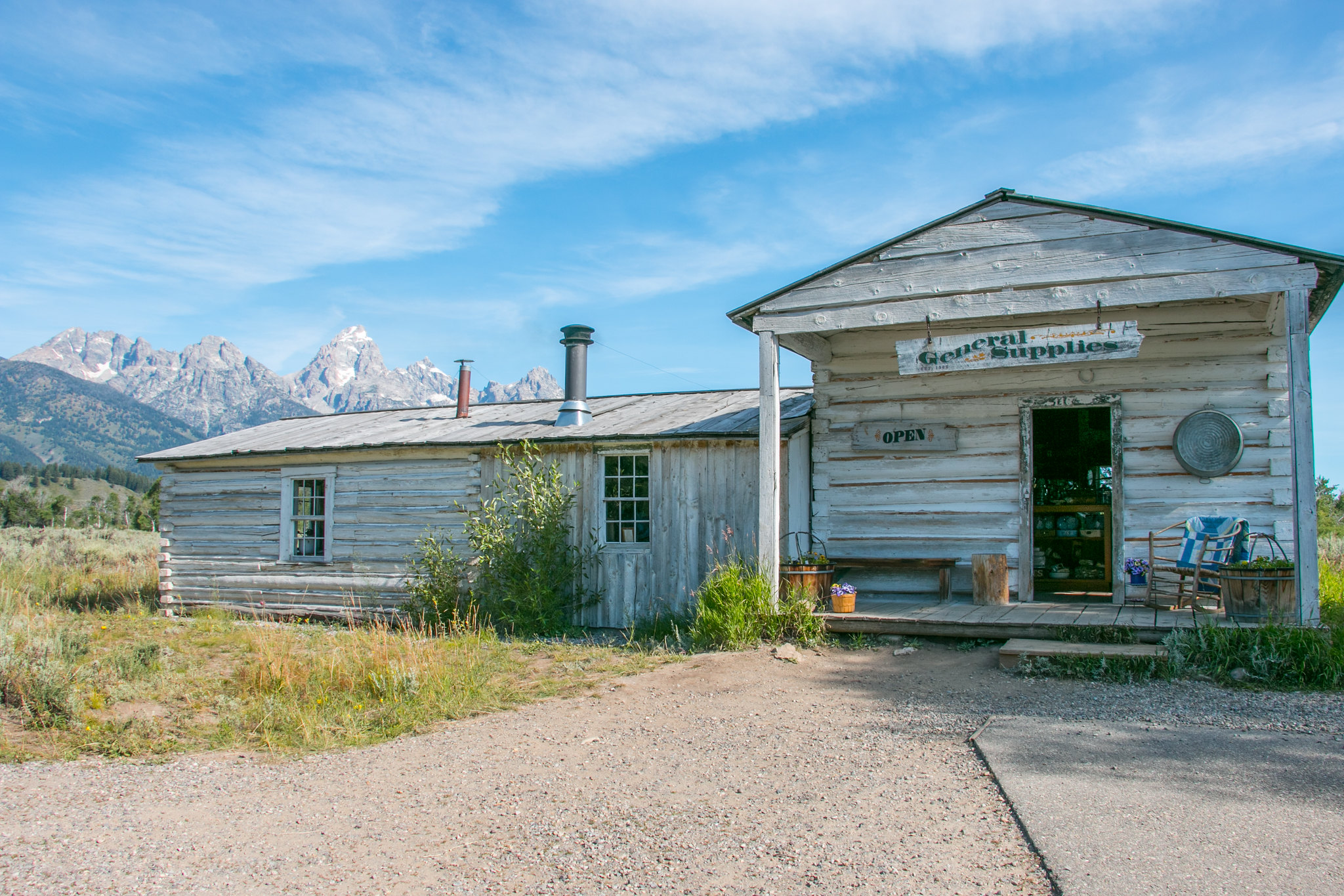 White clapboard and log building. Teton Range is in the distance.