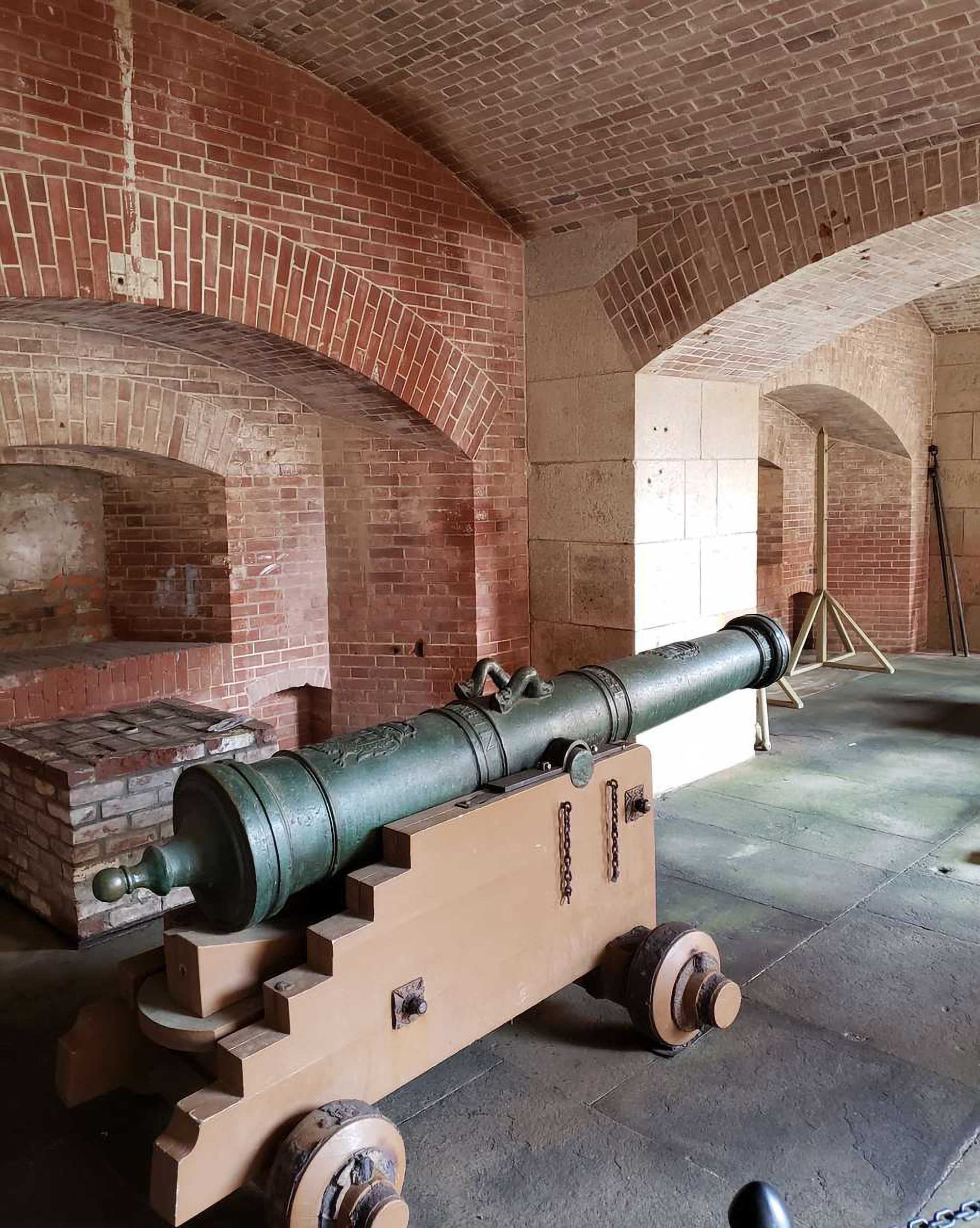 A cannon sits on a wooden cart inside the brick walls of Fort Point