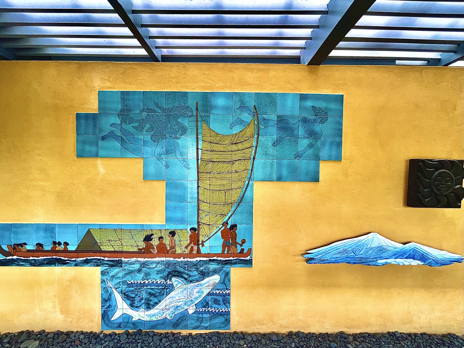 Mural showing paintings of polynesians sailing by canoe over a large shark painted in the water.