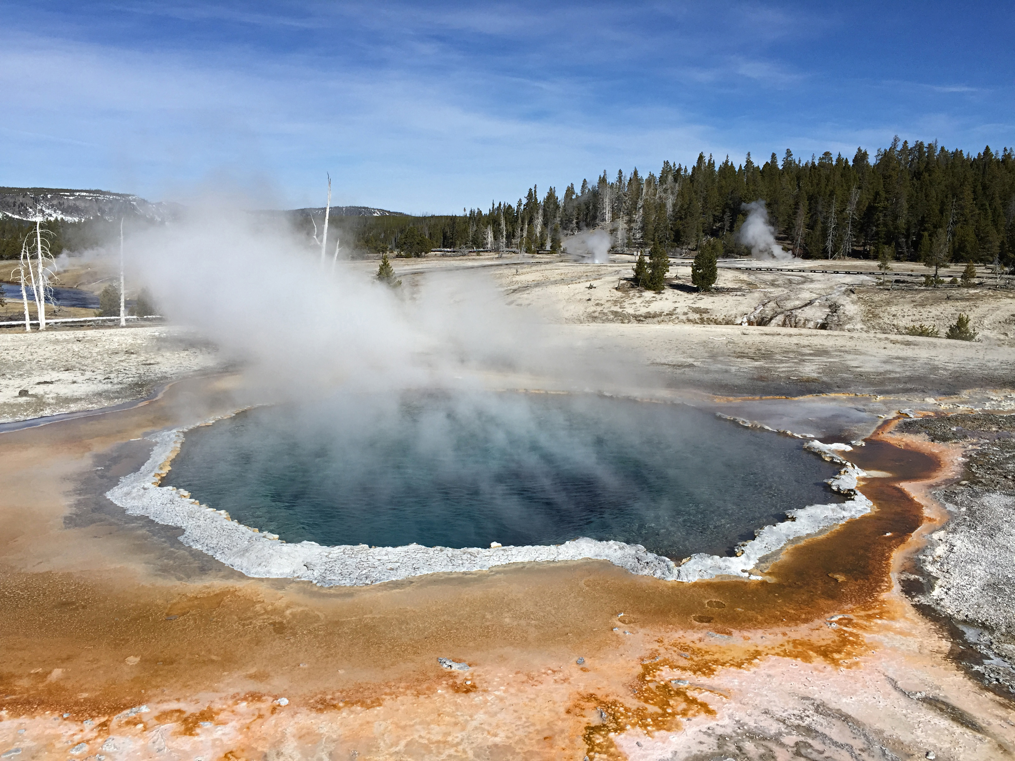 Steam rises from a circular, blue pool of water rimmed in white and orange.