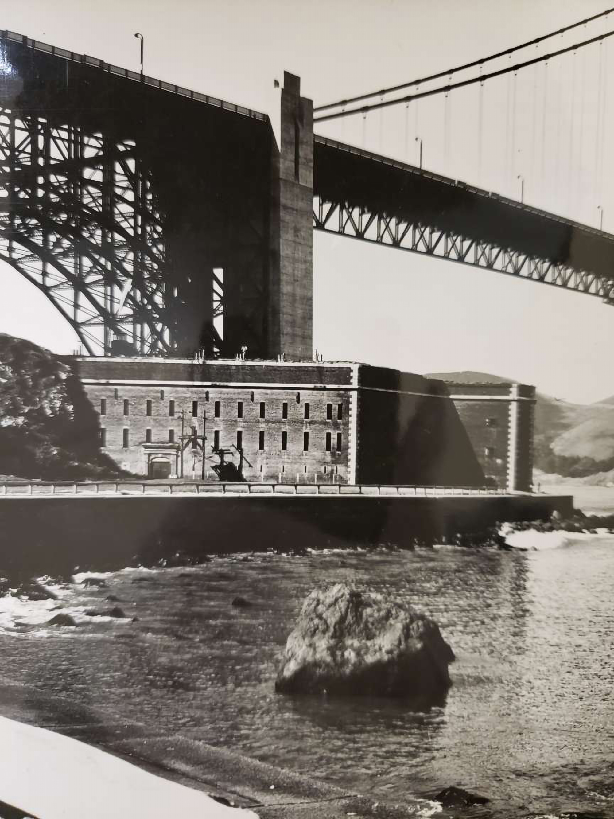 Black and white photo of the brick Fort Point as it sits below the Golden Gate Bridge