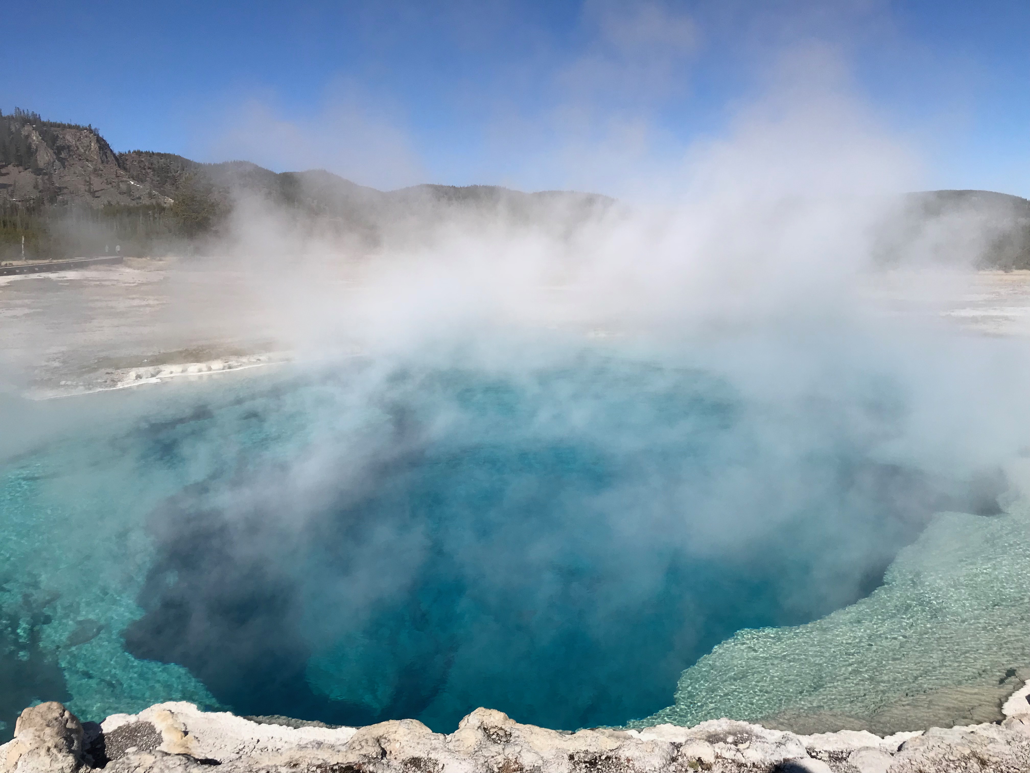 Steam rises from a deep, blue pool of hot water.