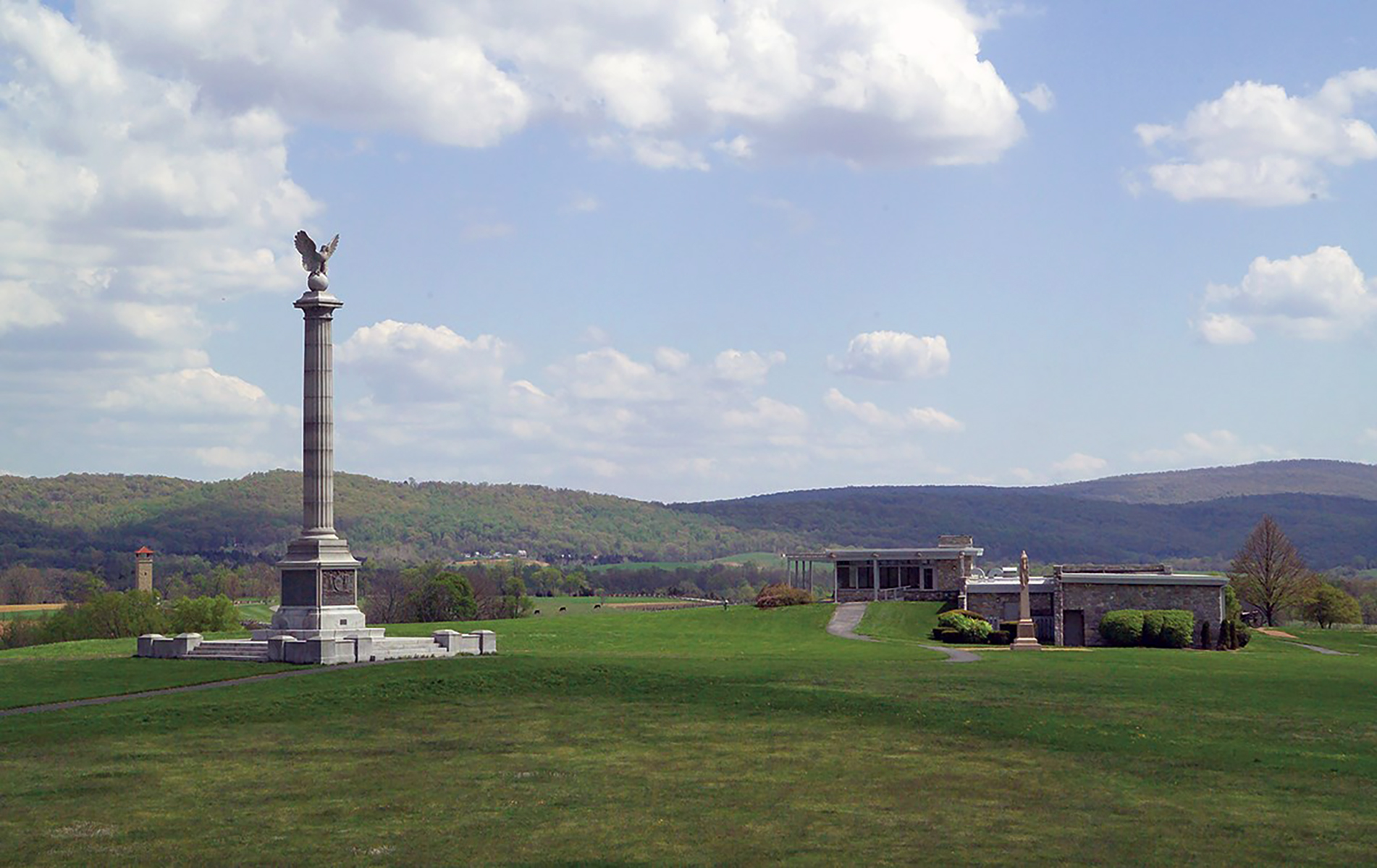 A grey statue on a lawn with a path leading to another statue and a building.