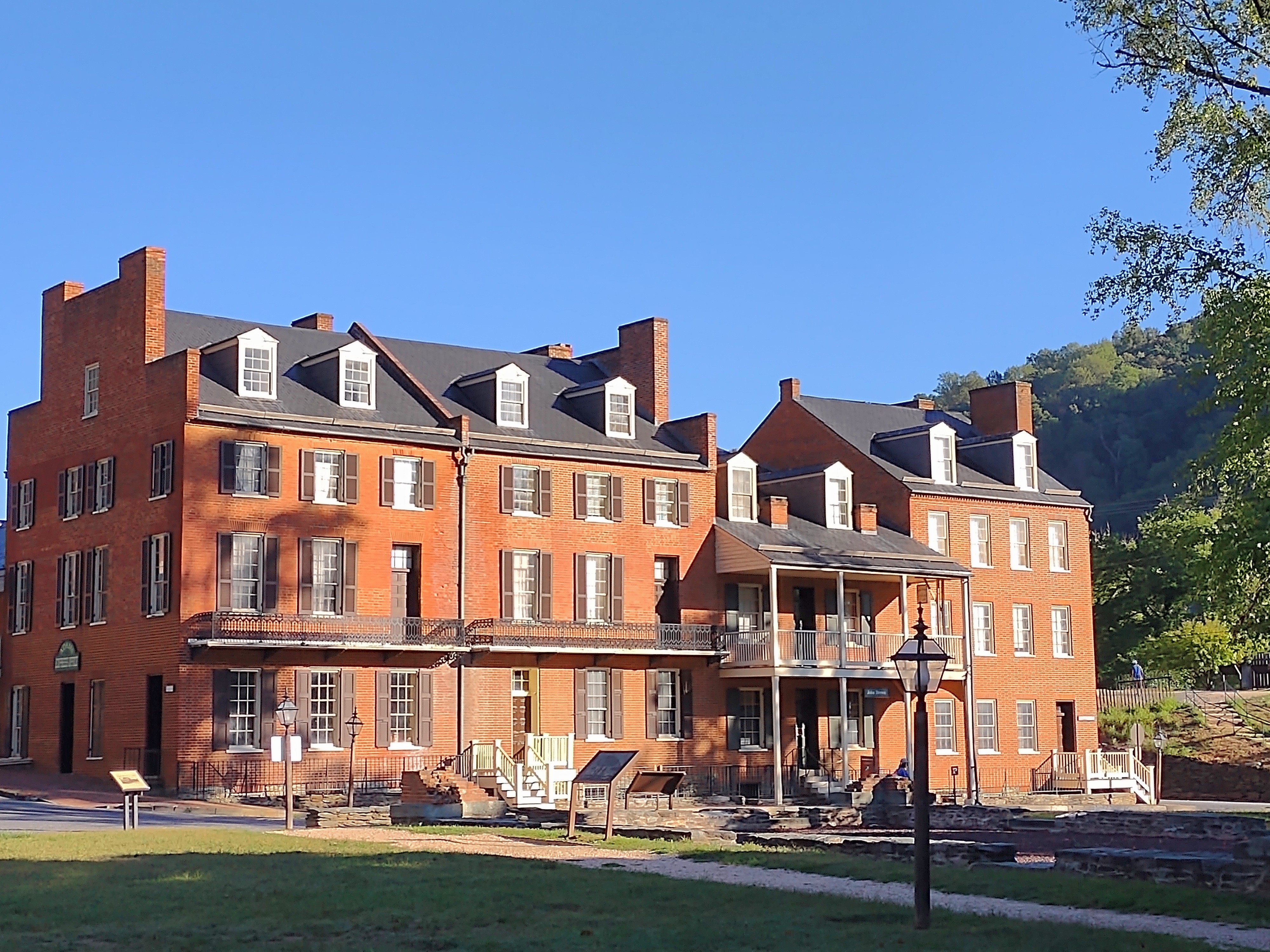 A row of large brick buildings stands along a street underneath a bright blue sky.