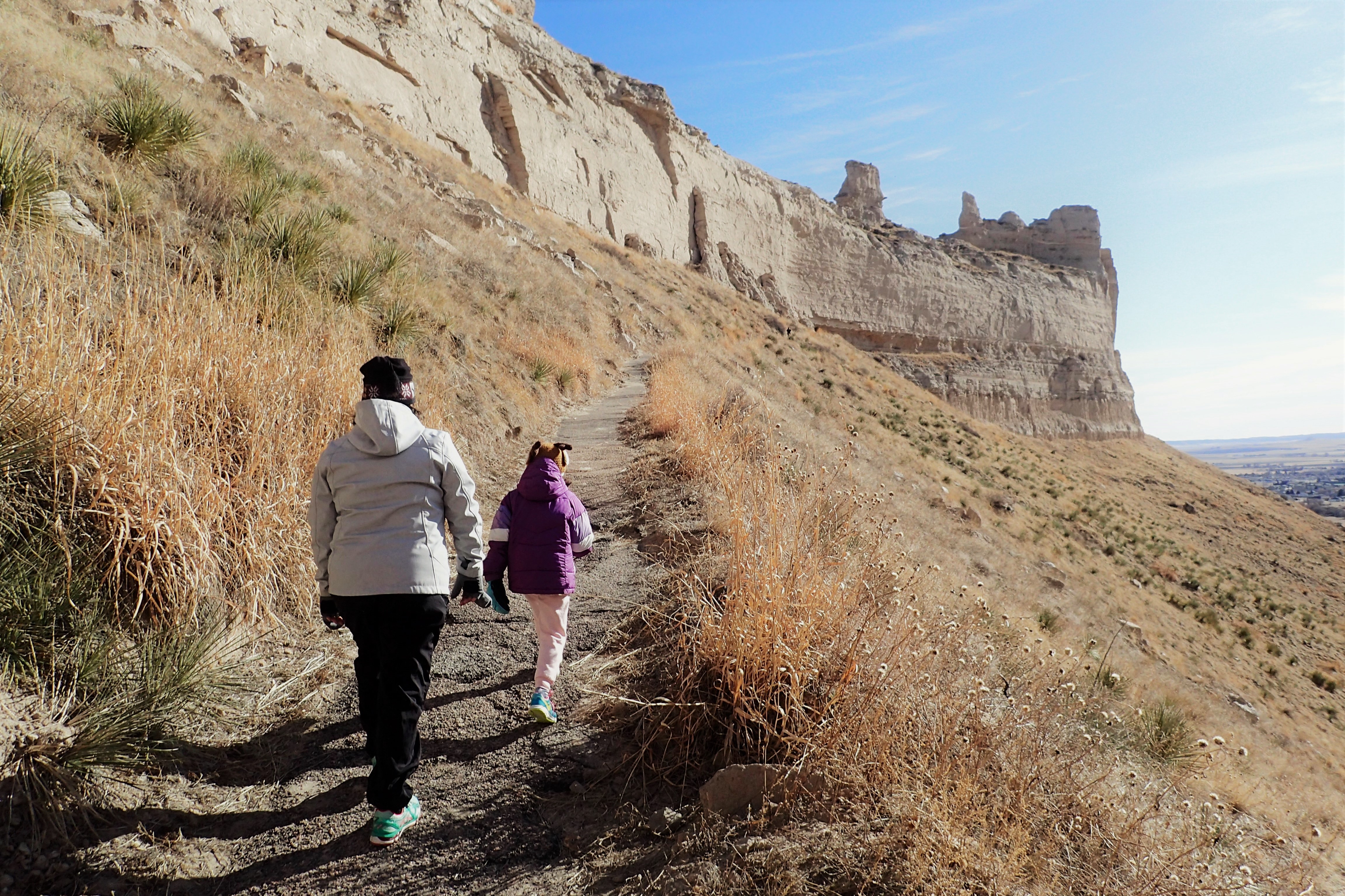 A pair of hikers ascends a paved walking trail up a sandstone bluff.