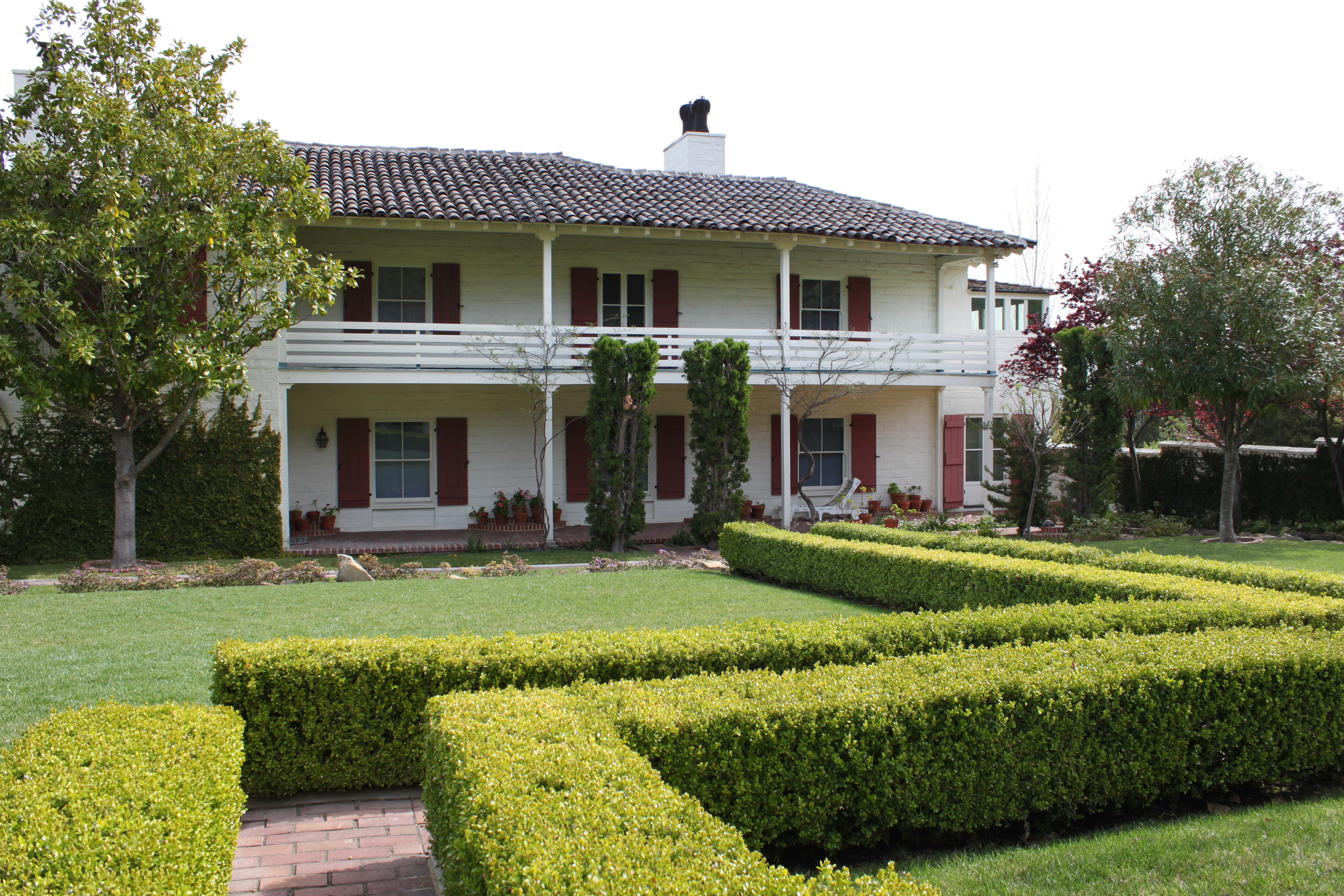 A two-story house with multiple windows can be seen with hedges and trees.