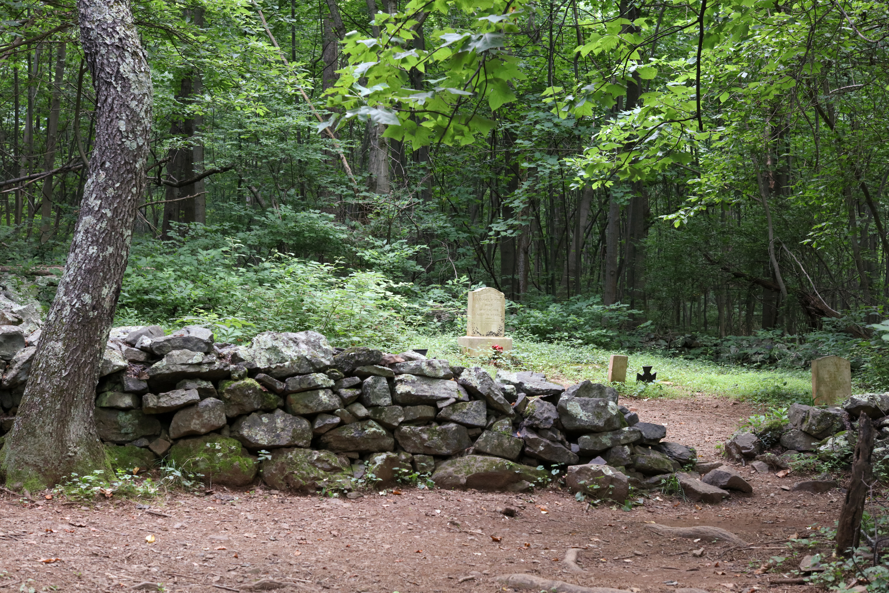 A small cemetery in the woods; stone fence; white gravestones