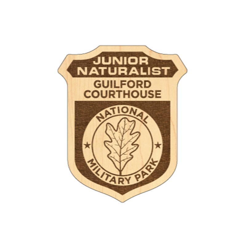 Tan wooden junior naturalist badge. It features the park name and the image of a leaf.